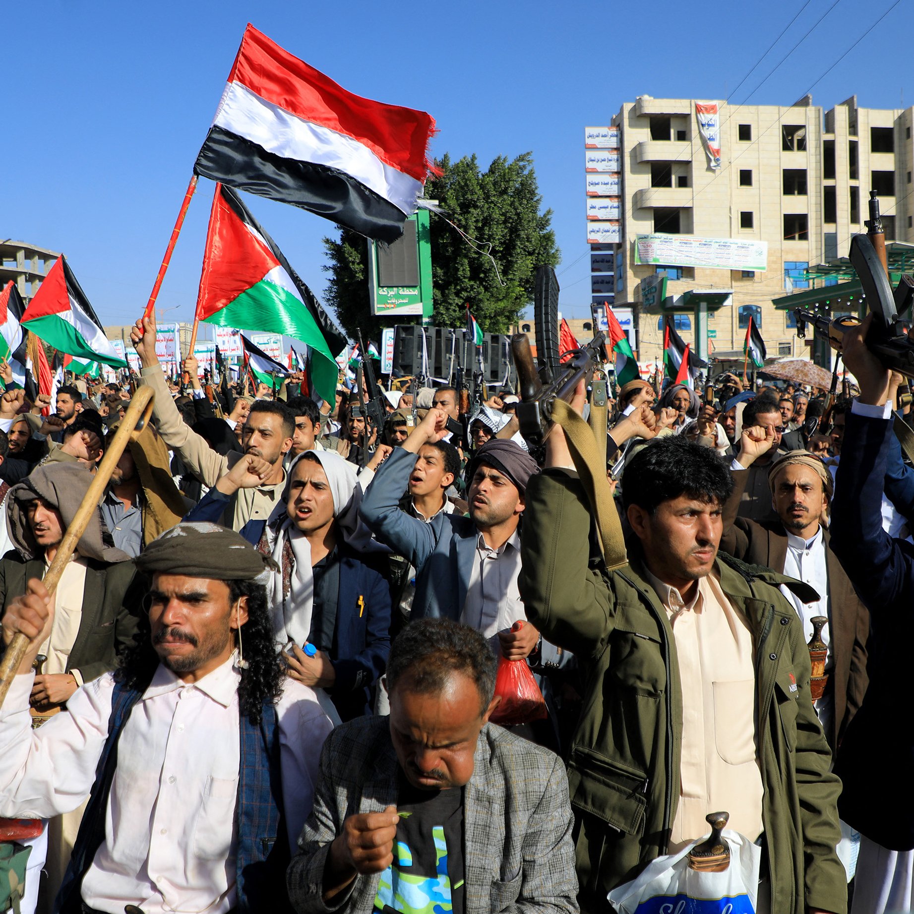 تظهر الصورة مجموعة من الأشخاص في تظاهرة حاشدة، يحملون الأعلام ويرتدون زيًّا تقليديًا. تعبر الوجوه عن الحماس وتظهر الأعلام التي تحمل ألوان الوطن. تتواجد خلفهم بنايات وبعض العلامات التجارية، مما يوحي بأن المكان هو منطقة حضرية. يبدو أن المتظاهرين يمارسون حقهم في التعبير عن آرائهم والمشاركة في حدث سياسي أو اجتماعي.