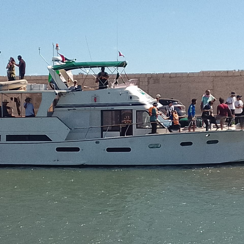 Un bateau à moteur blanc à quai, avec des passagers et un ciel bleu.