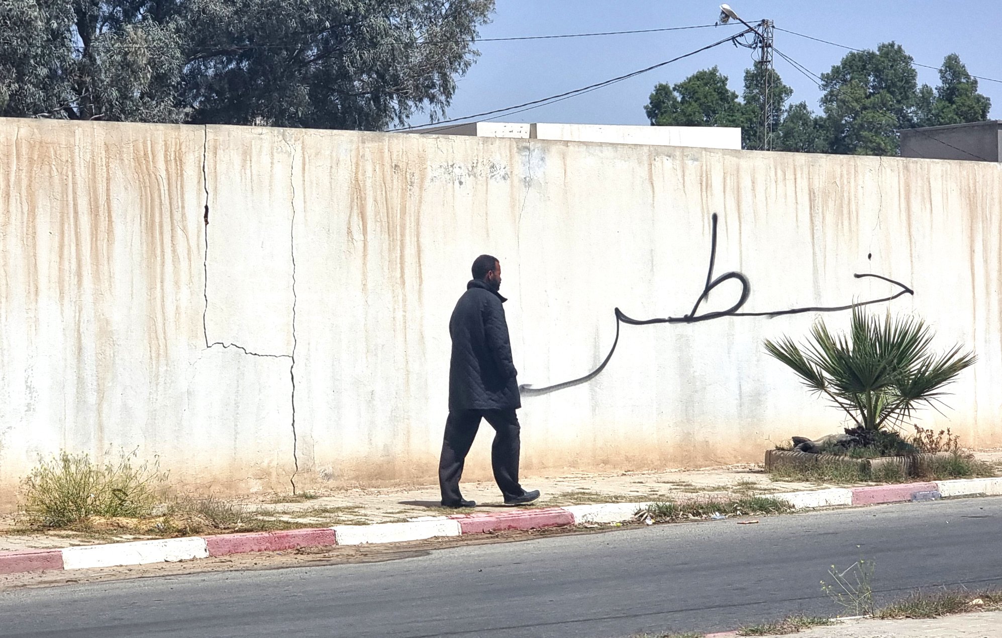 Un homme marche le long d'un mur avec une grande inscription en arabe.