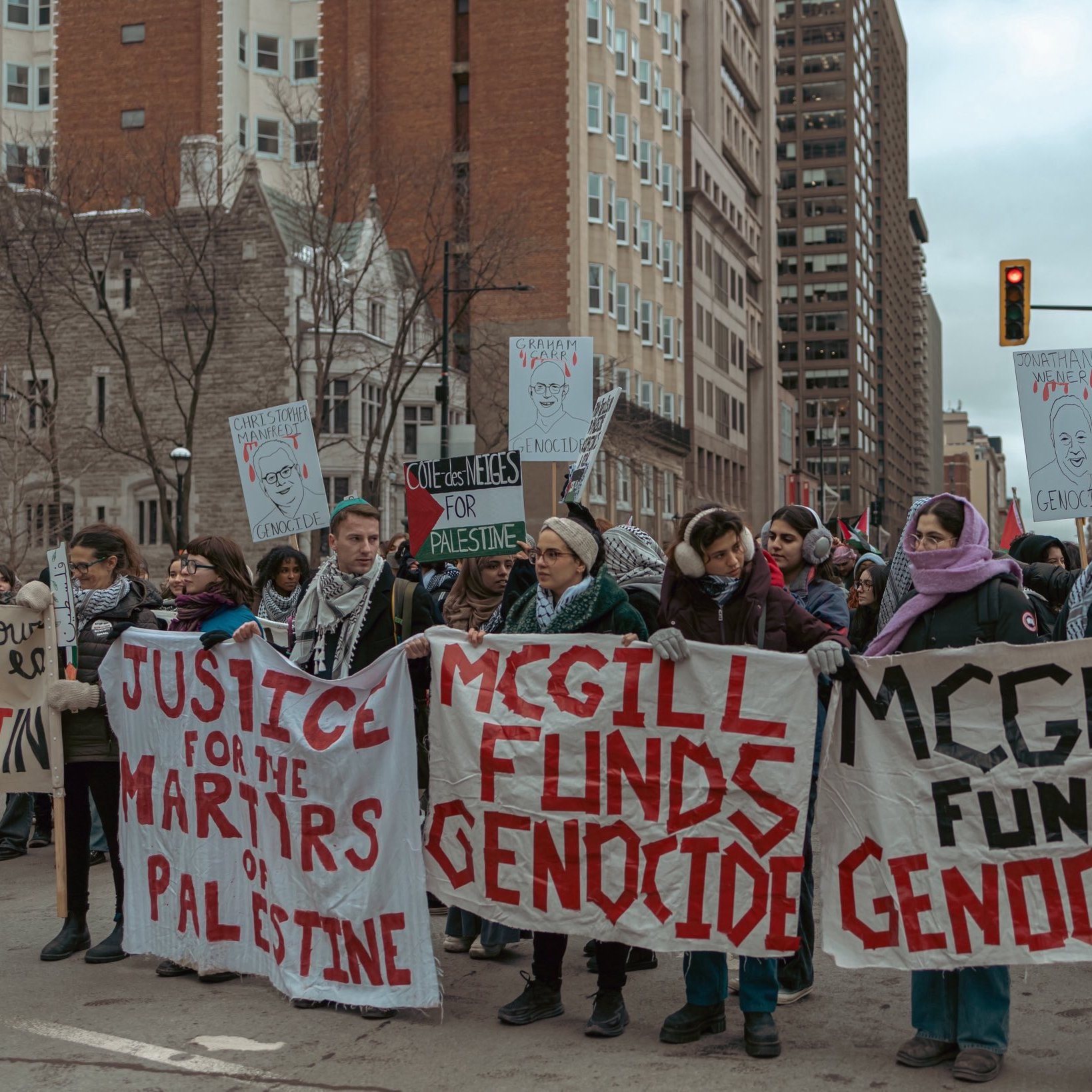 L'image montre une manifestation dans une ville urbaine. Un groupe de personnes est rassemblé, tenant des pancartes avec des messages en faveur de la Palestine et s'opposant au financement de ce qu'ils appellent un génocide. Certains manifestants portent des écharpes qui semblent indiquer leur solidarité avec la cause palestinienne. L'atmosphère est engagée et déterminée, avec des passants et des bâtiments en arrière-plan.