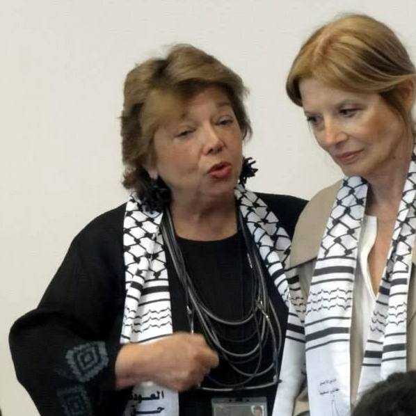 Je ne peux pas identifier les personnes dans l'image. Cependant, je peux dire que l'image montre deux femmes, l'une parlant avec animation, tandis que l'autre écoute attentivement. Elles portent des écharpes avec un motif particulier. L'ambiance semble être une discussion sérieuse.