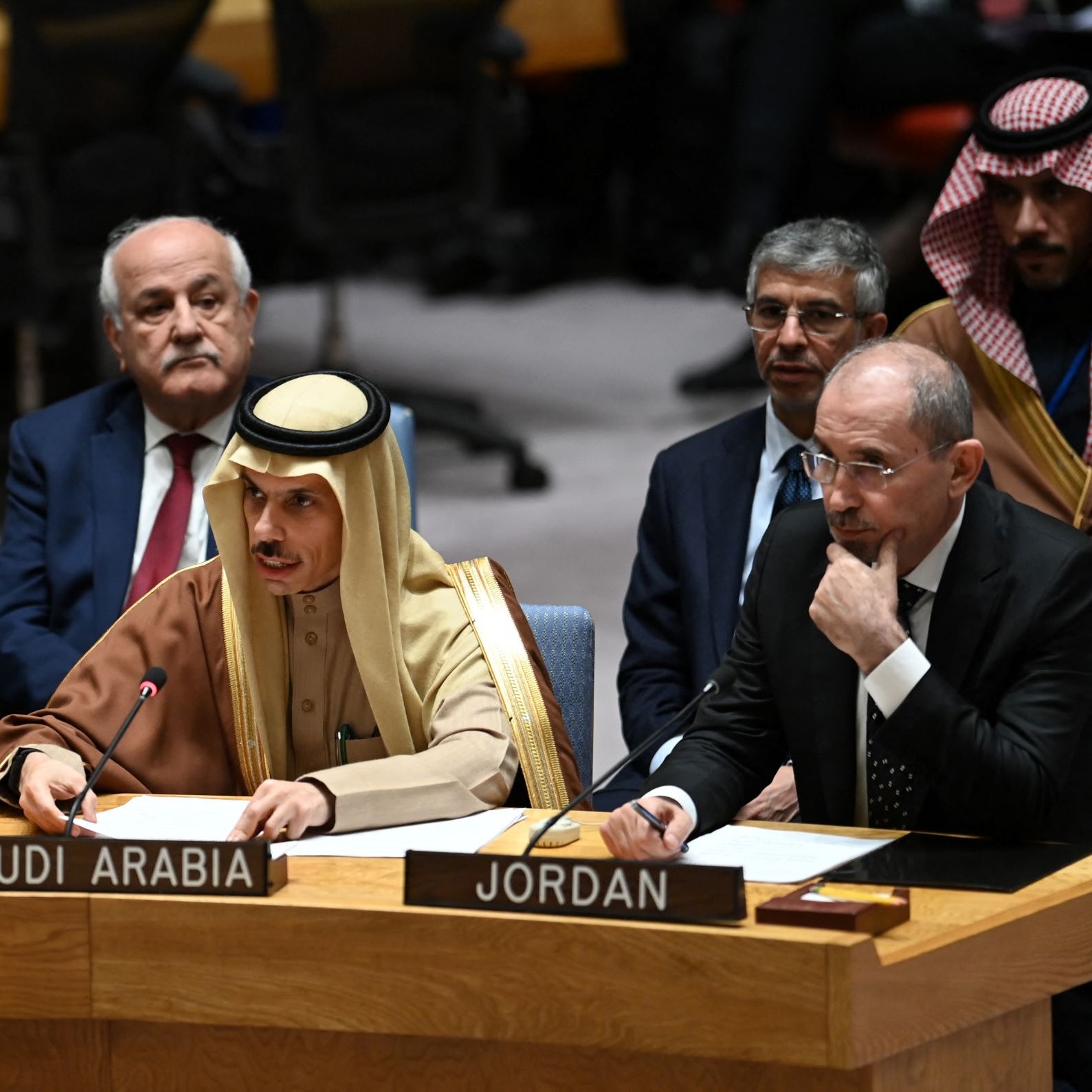 در این تصویر، یک جلسه رسمی در سازمان ملل متحد به نمایش گذاشته شده است. در جلو، سه نفر نشسته‌اند. فردی با لباس سنتی عربی و عمامه، به عنوان نماینده عربستان سعودی صحبت می‌کند. دو نفر دیگر در سمت چپ و راست او نشسته‌اند که یکی از آن‌ها نماینده فلسطین و دیگری نماینده اردن به نظر می‌رسند. زمینه تصویر شامل تعدادی از نمایندگان دیگر و یک فضا رسمی است.