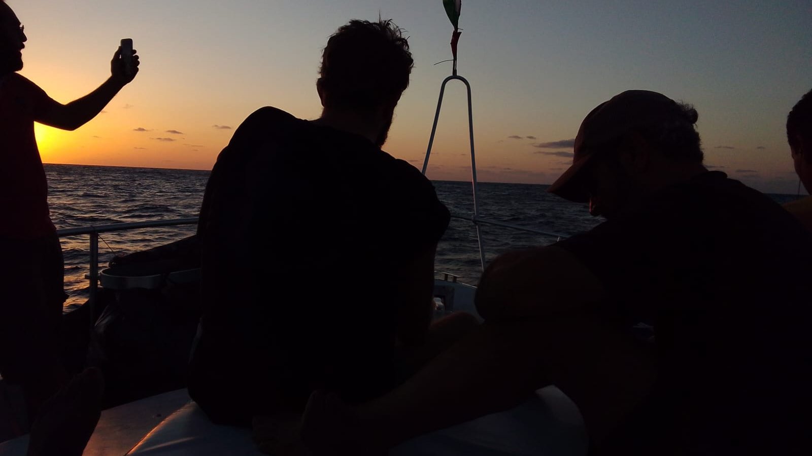 Silhouettes de personnes sur un bateau au coucher du soleil, mer calme.