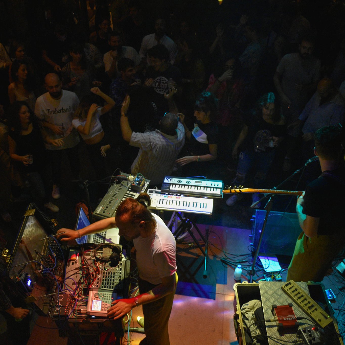 A lively concert scene with musicians using electronic instruments, surrounded by an energetic crowd.