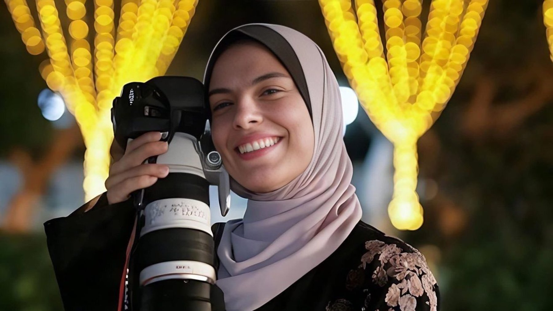 Jeune femme souriante avec un appareil photo, entourée de lumières scintillantes.