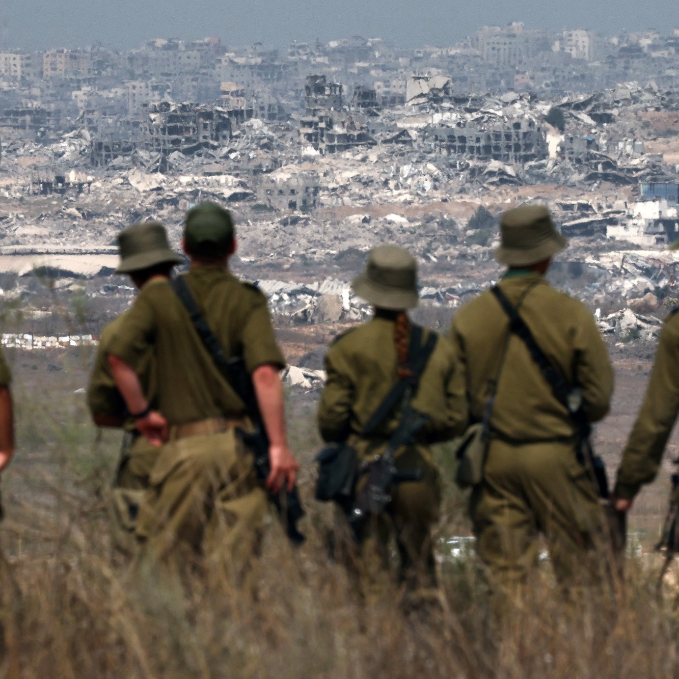Des soldats en uniforme observant des ruines de bâtiments en arrière-plan.
