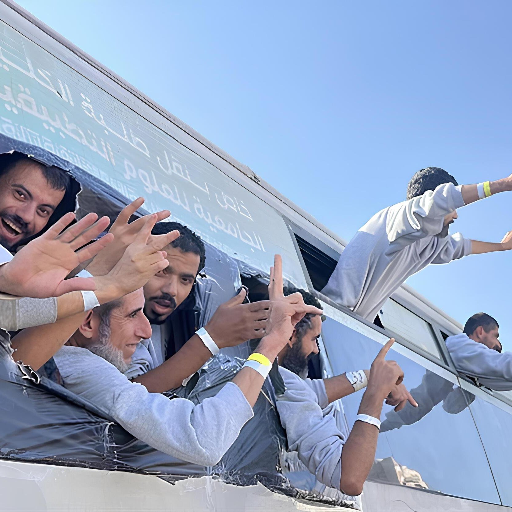Gruppo di persone sorridenti sporge da un bus con le mani alzate, in un'atmosfera festosa.