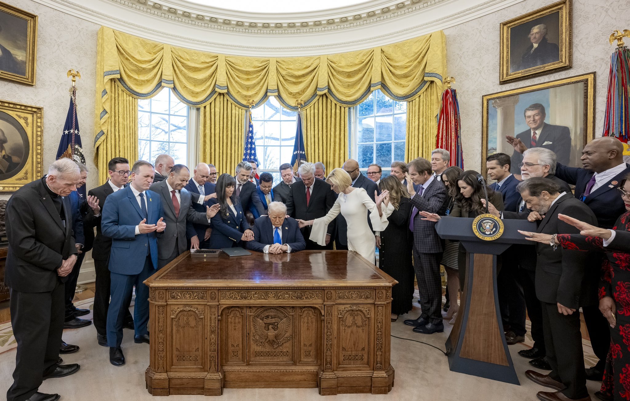 اجتماع رسمي في المكتب البيضاوي مع أشخاص حول طاولة، والدنيا مضاءة خلفهم.