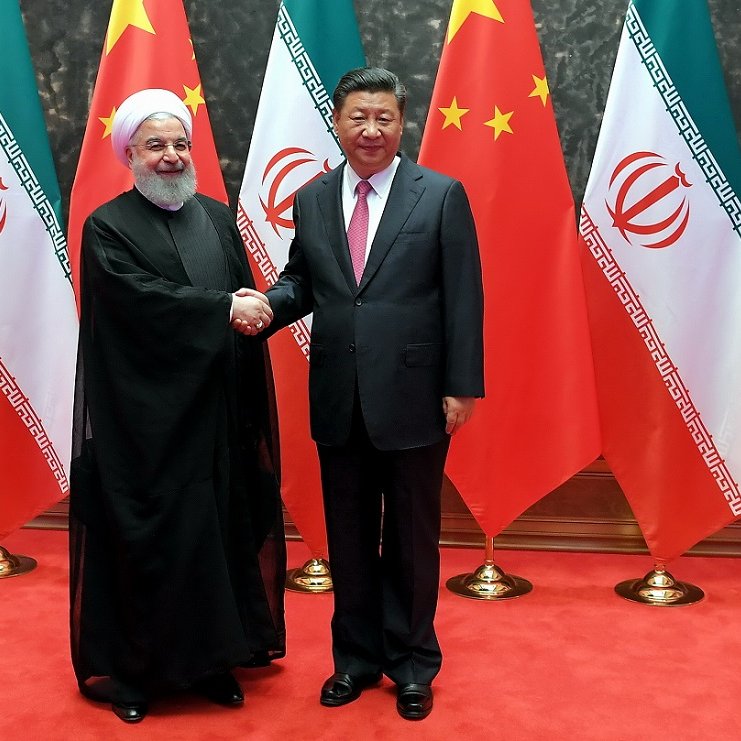 L'image montre deux dirigeants se serrant la main, souriant, devant un fond composé de drapeaux. À gauche, une figure en habit traditionnel noir, probablement d'origine iranienne, et à droite, un homme en costume sombre avec une cravate rouge, représentant probablement la Chine. Le décor inclut des drapeaux chinois et iraniens, soulignant une rencontre diplomatique entre les deux pays. Le tapis rouge au sol ajoute une touche officielle à l'événement.