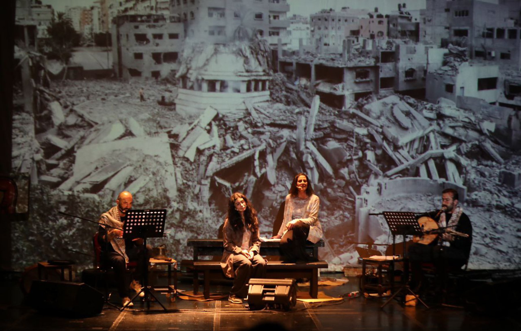Quatre artistes sur scène, avec une projection d'un paysage de destruction en arrière-plan.