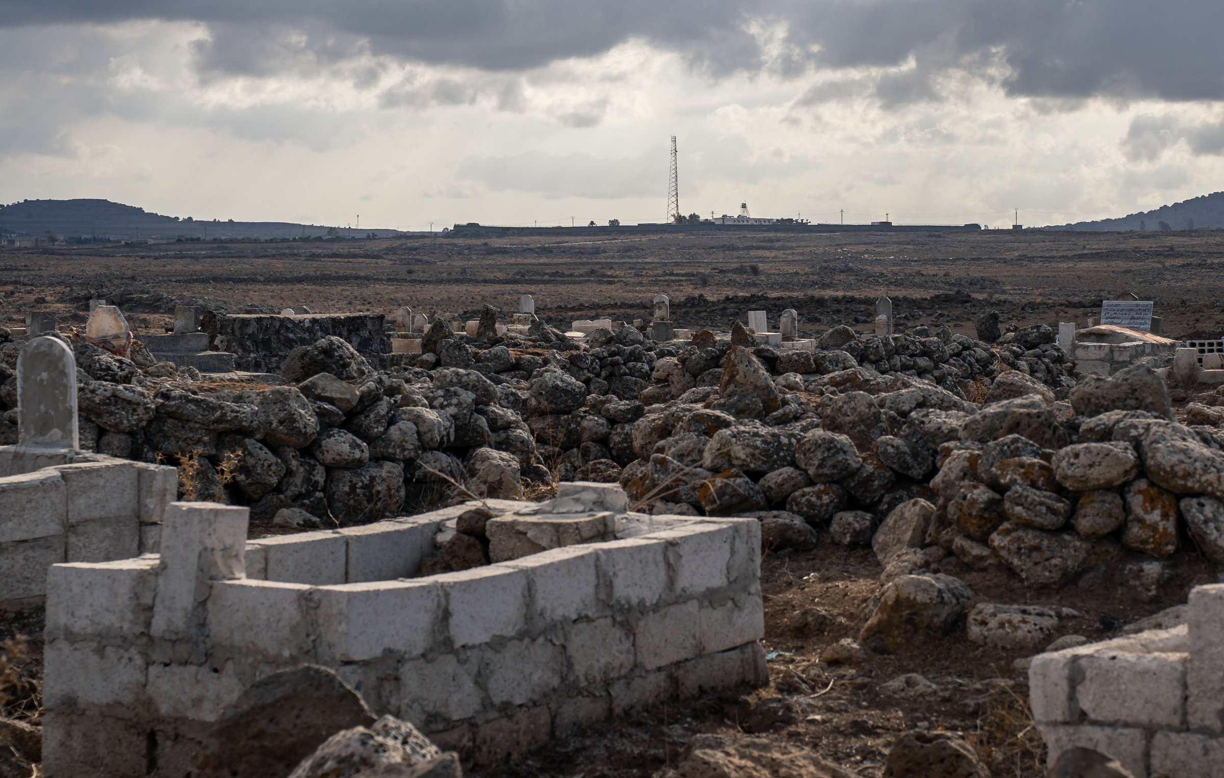 Un paysage aride avec des tombes et des pierres, sous un ciel nuageux.