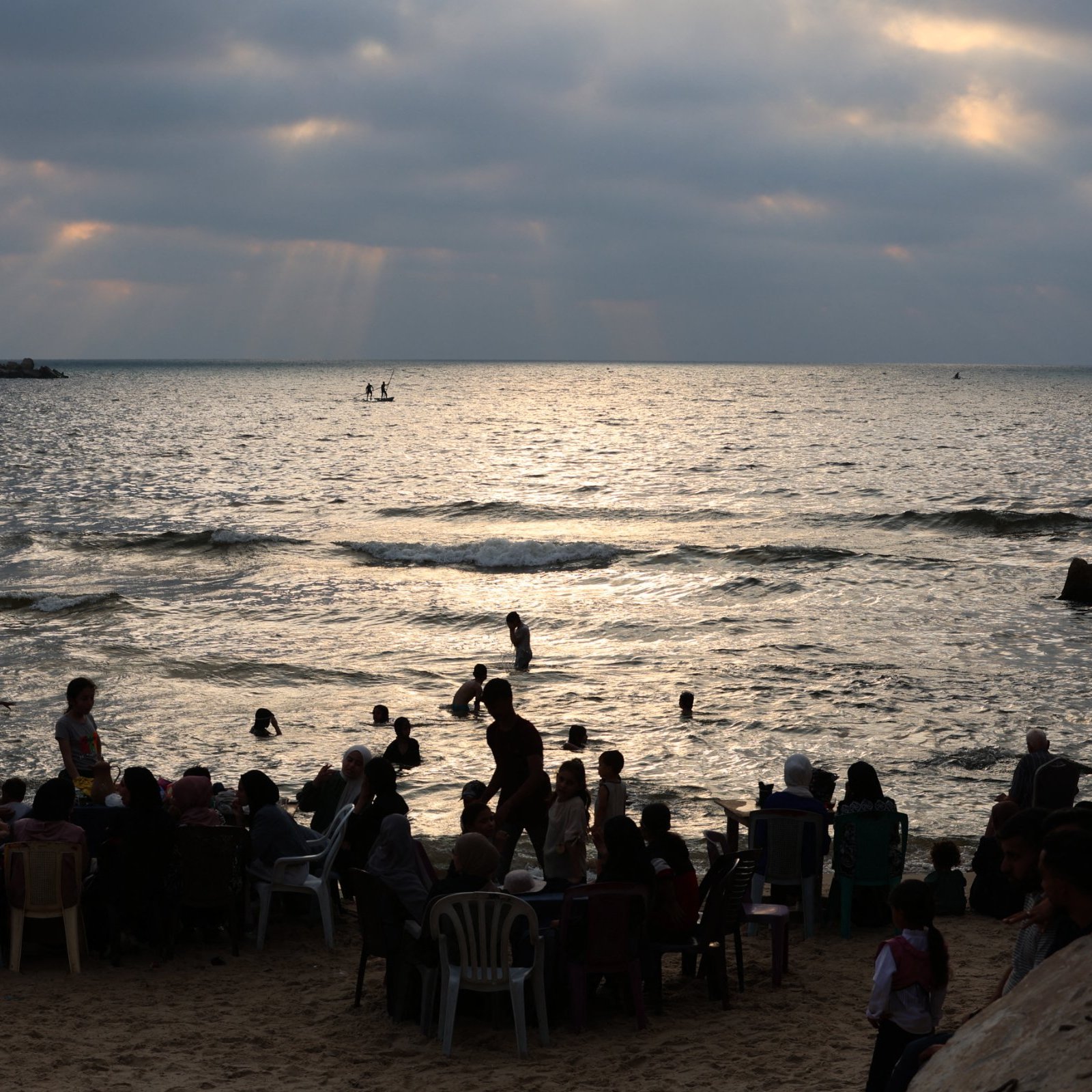 Plage animée au crépuscule, avec des gens dans l'eau et sur le sable.