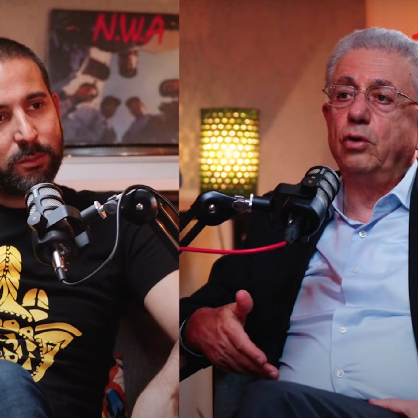 في الصورة، يظهر شخصان يجلسان معاً، يتحدثان، وأمام كل منهما ميكروفون.