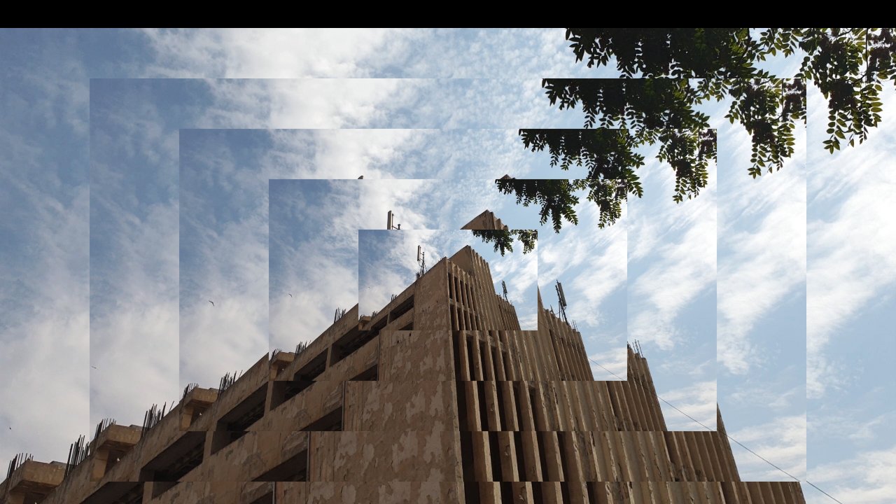 تظهر الصورة مشهداً لمبنى معاصر يظهر فيه تصميم معماري مميز، حيث يتكون المبنى من عدة طبقات وأشكال هندسية واضحة. السماء خلف المبنى محاطة بسحب بيضاء متناثرة، مما يضيف جمالاً إلى المشهد. في الزاوية العليا، هناك مجموعة من الأوراق الخضراء لشجرة تضفي لمسة طبيعية على الصورة. التصميم يبدو مزيجاً من الحداثة والطبيعة، مما يخلق تبايناً جميلاً بين العمارة والبيئة المحيطة.