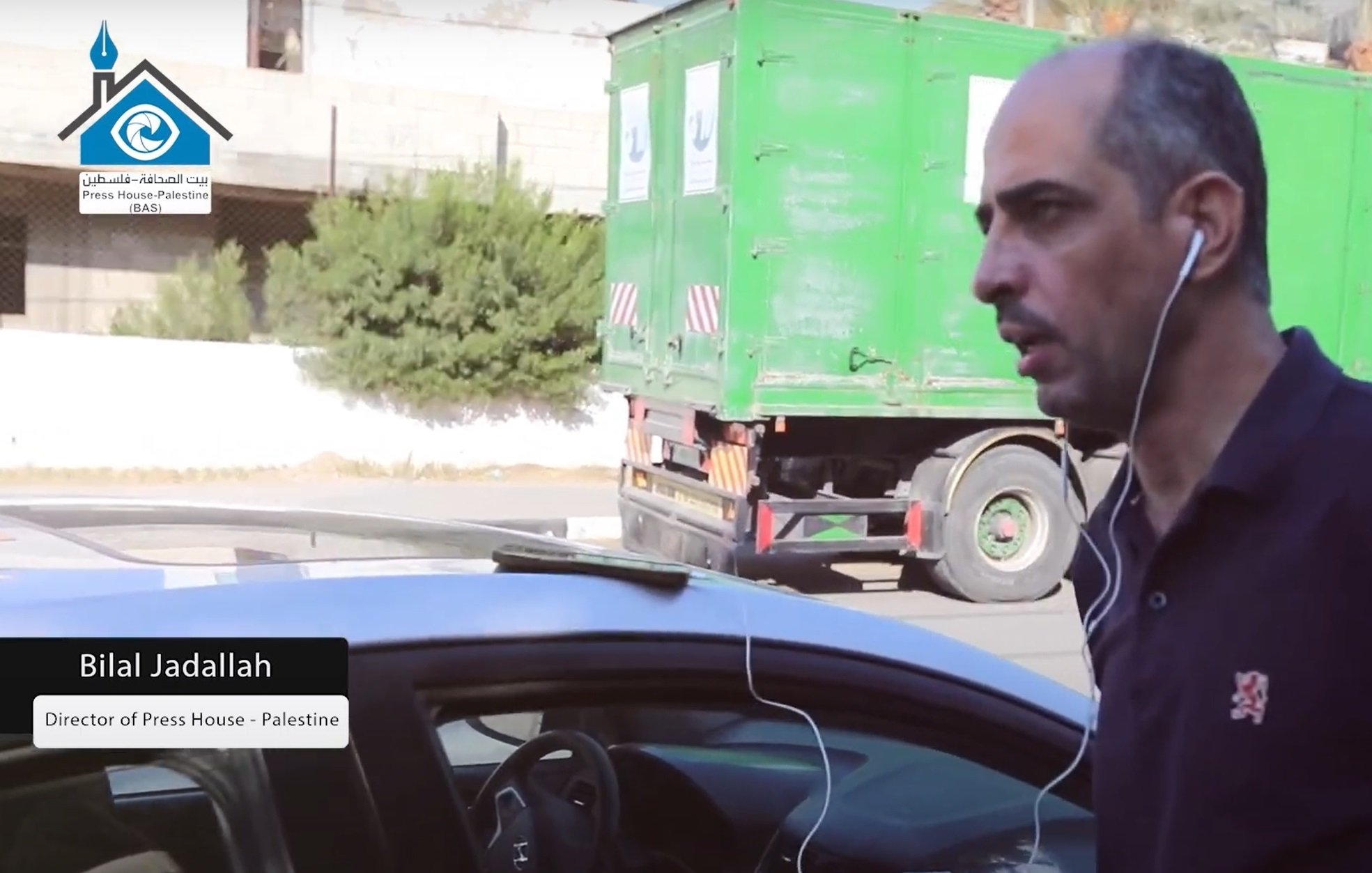 در این تصویر، مردی به نام بیلا الجدلله دیده می‌شود که ظاهراً مدیر خانه مطبوعات در فلسطین است. او در حال حرکت در یک خیابان است و هدفون‌هایی به گوش دارد. در پس‌زمینه یک کامیون سبز رنگ قرار دارد. این تصویر به وضوح زندگی روزمره و فعالیت‌های فردی او را نشان می‌دهد.