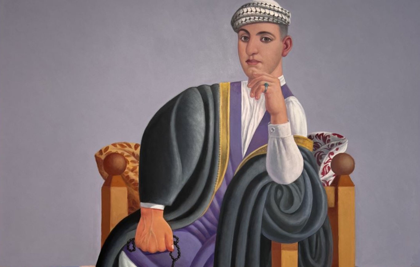 Un homme assis, vêtu traditionnellement, sur une chaise, avec un tapis coloré en dessous.