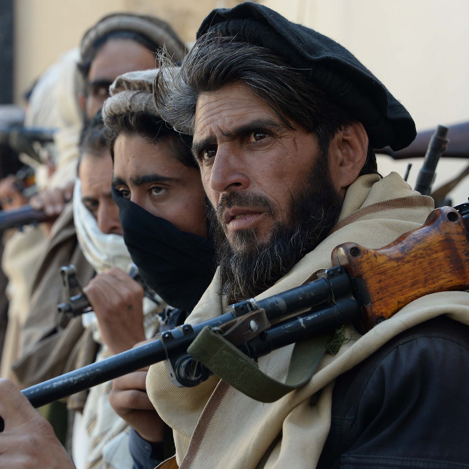 تظهر الصورة مجموعة من الرجال يقفون في صف، يحمل كل منهم سلاحًا. معظمهم يرتدي ملابس تقليدية، ويبدو عليهم الجدية والتركيز. يتواجد في الخلفية مجموعة من الأشخاص أيضًا، ويبدو أن الصورة تلتقط لحظة توتر أو استعداد. الخلفية غير واضحة ولا تحتوي على تفاصيل كثيرة.