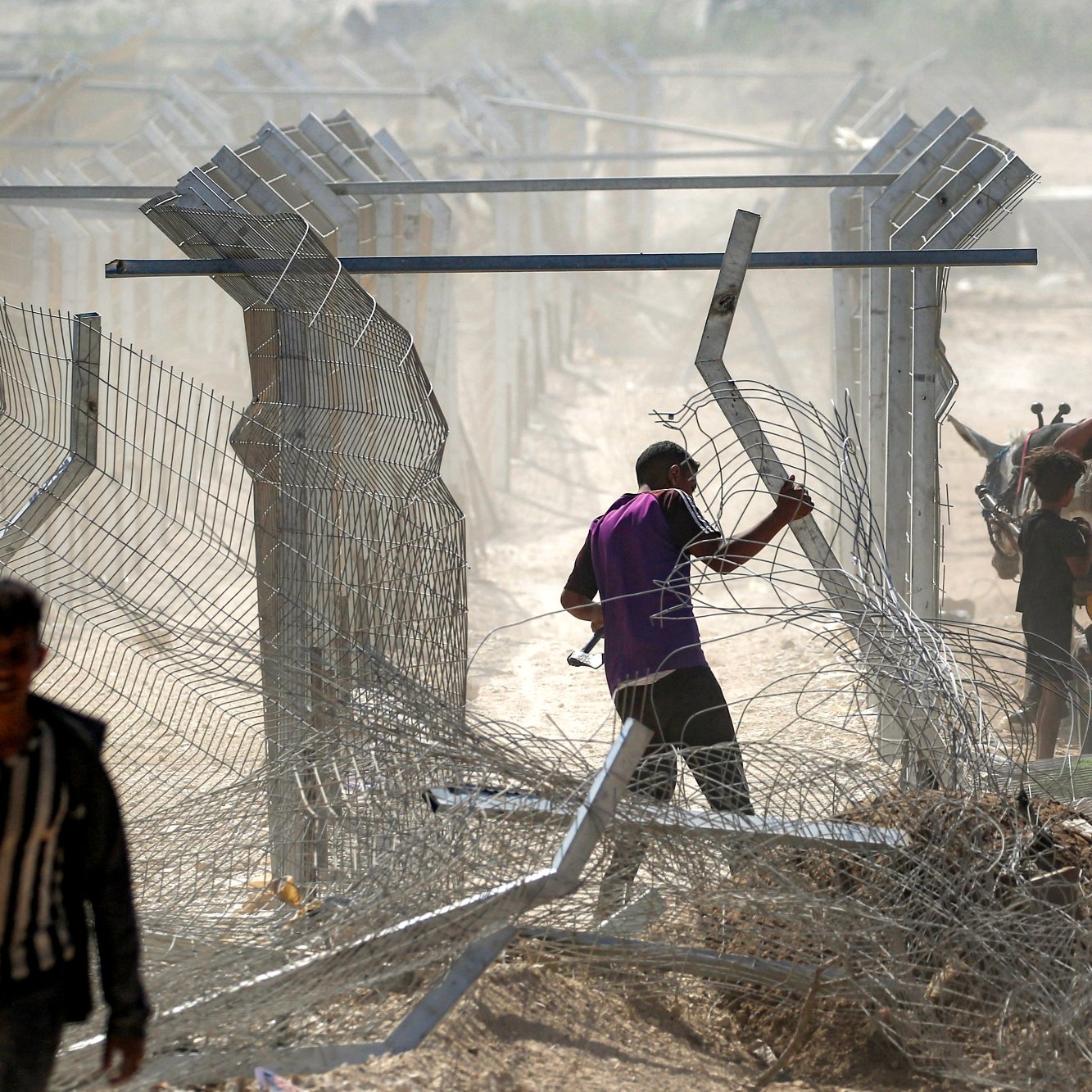 Uomini vicino a una recinzione di filo spinato in un'area polverosa e confusa.
