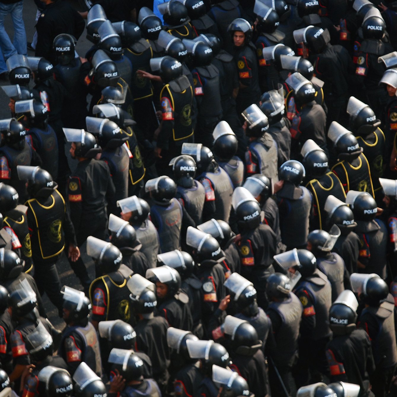 L'image montre un grand groupe de policiers en tenue d'émeute. Ils portent des casques et des boucliers, et sont regroupés de manière organisée. Les uniformes sont sombres, avec des détails visibles tels que des insignes ou des logos indiquant leur affiliation. L'ensemble donne une impression de préparation et de contrôle, évoquant un contexte de maintien de l'ordre lors d'une situation potentiellement tendue.
