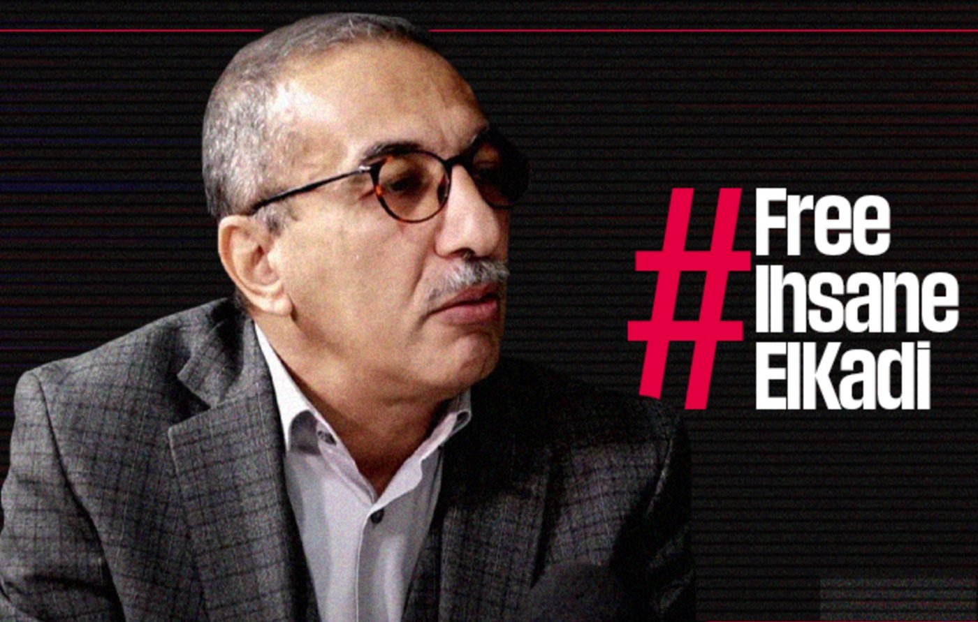 L'image montre un homme portant des lunettes et un costume à carreaux. Il semble participer à une interview ou à un débat, étant tourné vers un interlocuteur. À côté de lui, le texte en gras indique "#Free Ihsane ElKadi", suggérant qu'il est lié à une campagne de sensibilisation ou de soutien pour cette personne. L'arrière-plan présente un design graphique sobre, probablement pour mettre en avant le message.