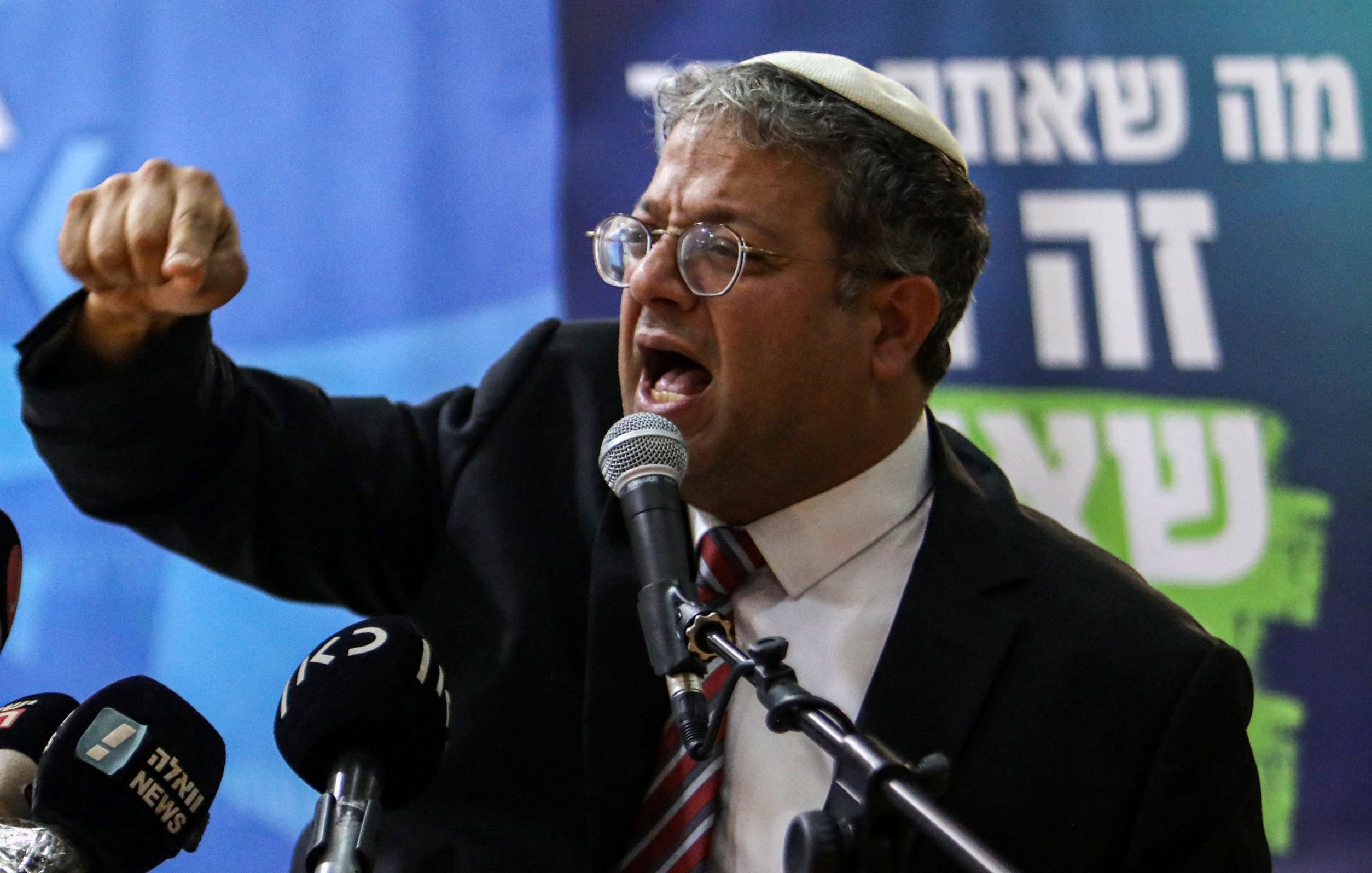 در این تصویر، یک مرد با عینک و کلاهی روی سر در حال صحبت کردن است. او به میکروفون نزدیک شده و به نظر می‌رسد که passionately در حال بیان نقطه نظری است. در پس‌زمینه، تعدادی لوگو و نوشته‌های مربوط به رسانه‌ها دیده می‌شوند. به نظر می‌رسد این نشست یا سخنرانی از اهمیت خاصی برخوردار باشد.