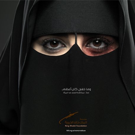 L'image montre une femme portant un niqab, couvrant la majeure partie de son visage. Ses yeux sont mis en valeur, l'un d'eux ayant un maquillage sombre, tandis que l'autre semble plus clair. Cette composition crée un contraste saisissant. En bas de l'image, il y a un texte en arabe et le logo de la Fondation King Khalid. L'image semble porter un message puissant et engageant.