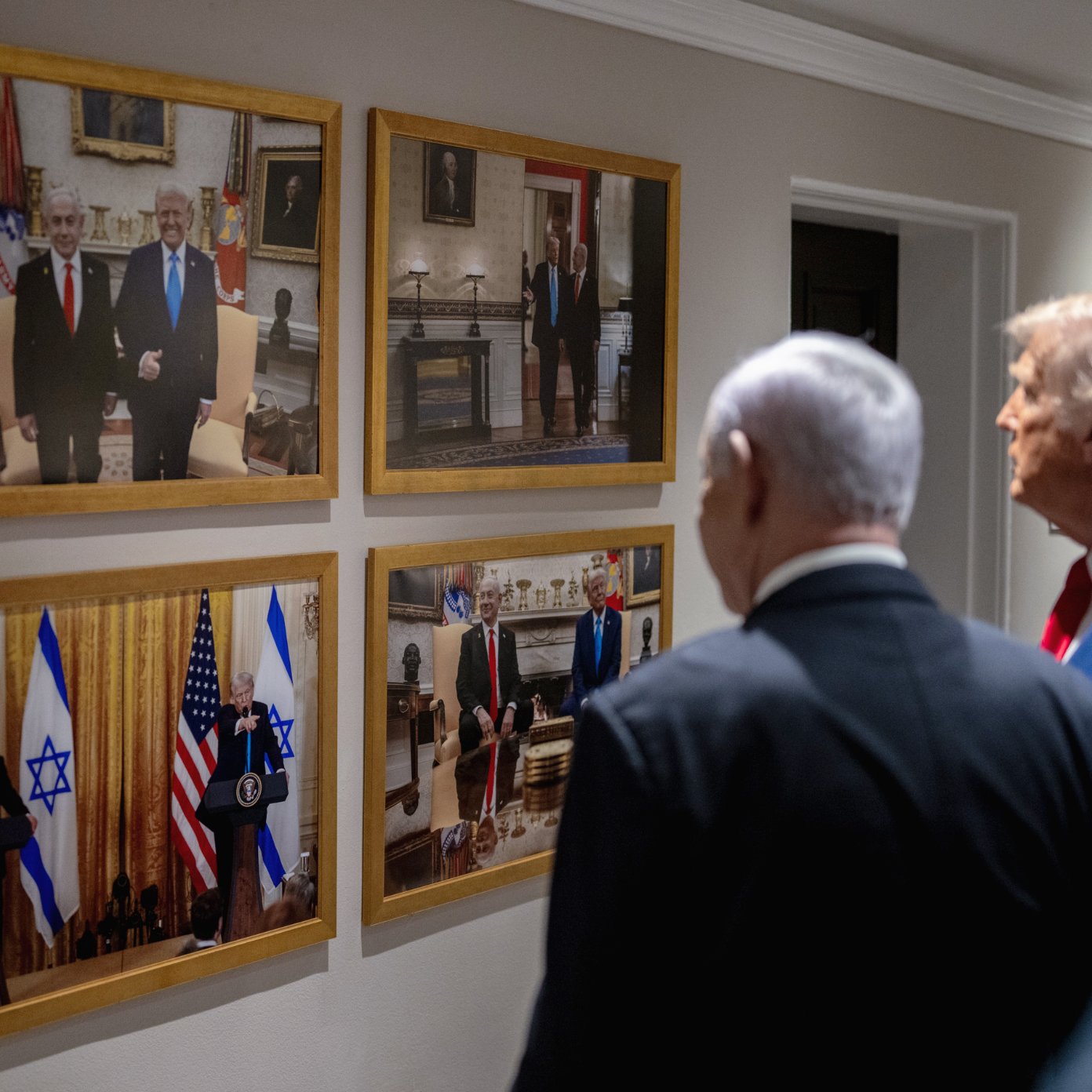 دو مرد در کت و شلوار در کنار یکدیگر ایستاده‌اند. تصاویر آن‌ها بر دیواری قاب شده‌اند.