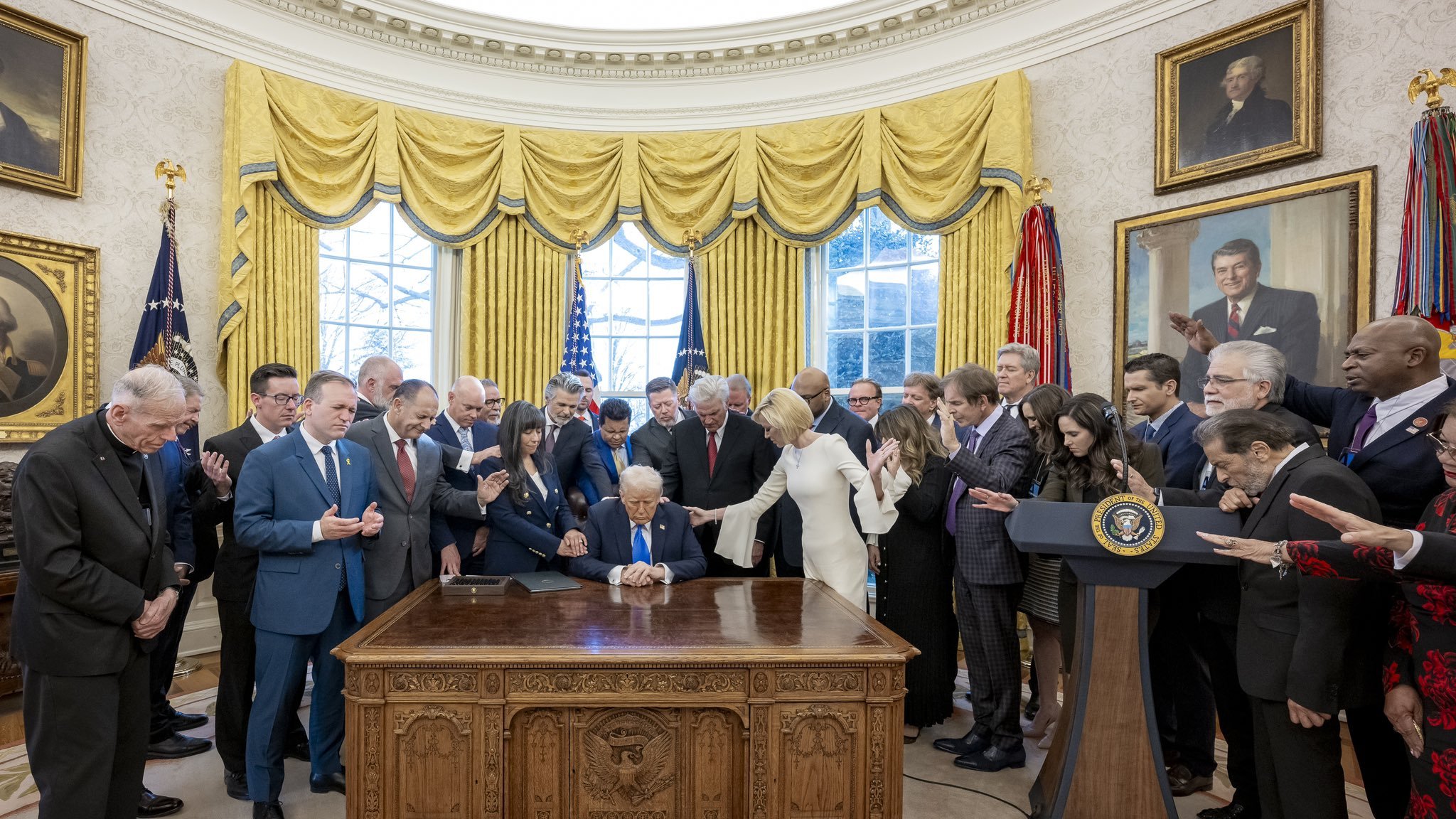 اجتماع رسمي في المكتب البيضاوي مع أشخاص حول طاولة، والدنيا مضاءة خلفهم.