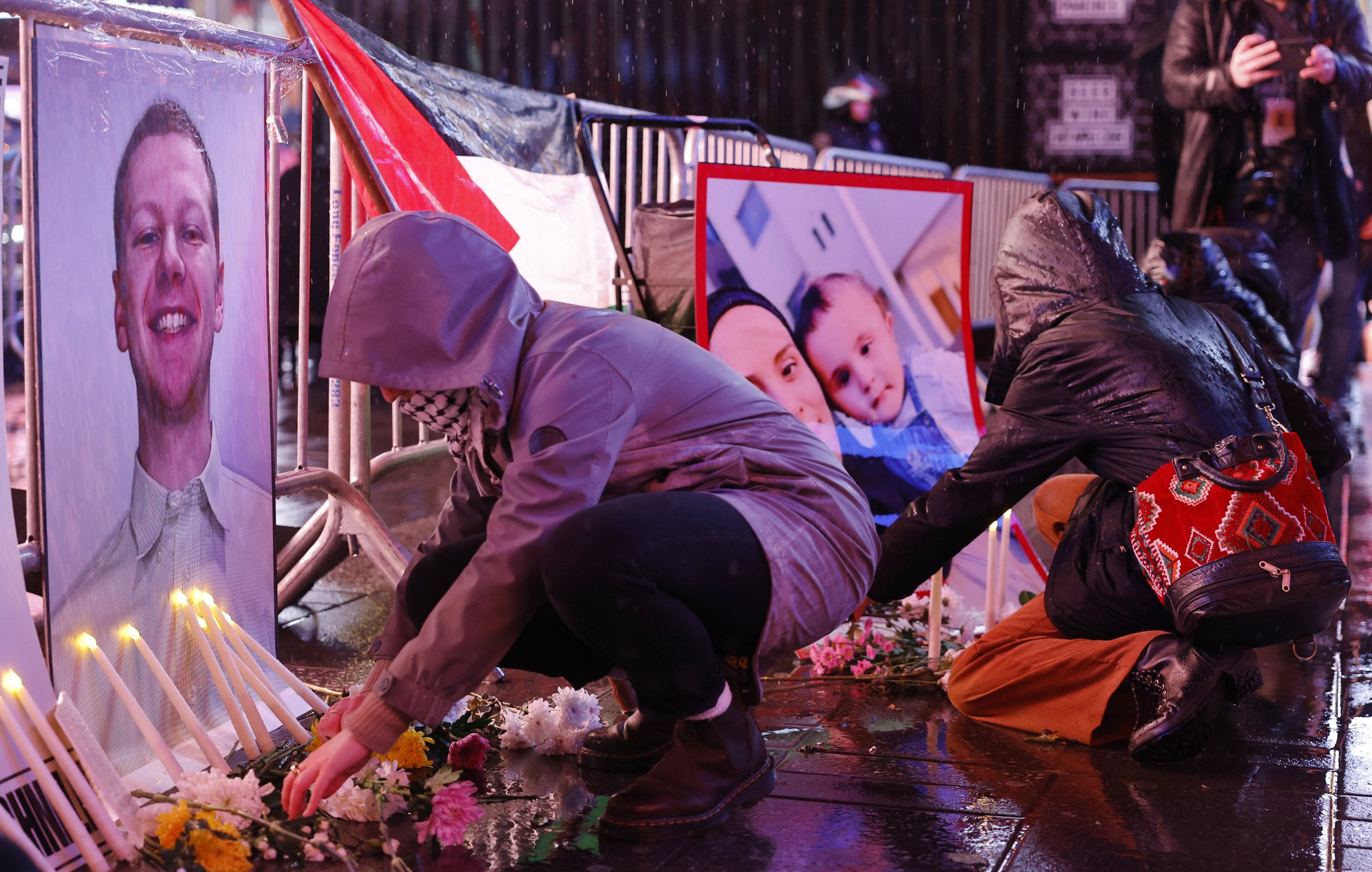 تصویر فضای یک تجمع یادبود را نشان می‌دهد که در آن افراد در حال قرار دادن شمع و گل هستند. در جلوی آنها، تصاویری از یک فرد و یک خانواده به نمایش گذاشته شده است. باران به زمین می‌ریزد و خیابان براق است. افراد با لباس‌های گرم و کلاه روی زمین نشسته‌اند و به یاد افرادی که از دست رفته‌اند، مراسمی برگزار می‌کنند. این صحنه حال و هوای غم و اندوه را منتقل می‌کند.