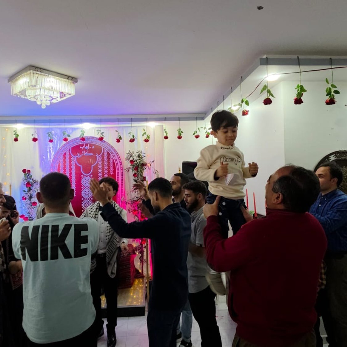 Fête joyeuse avec des gens dansant, décorations florales et un enfant porté.