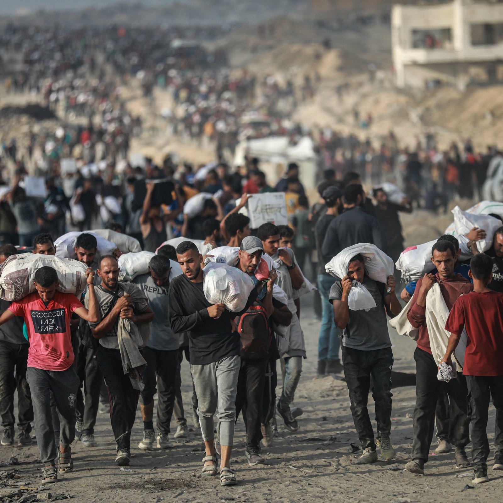 Des personnes marchent en masse, portant des charges sur leurs épaules, dans un environnement difficile.