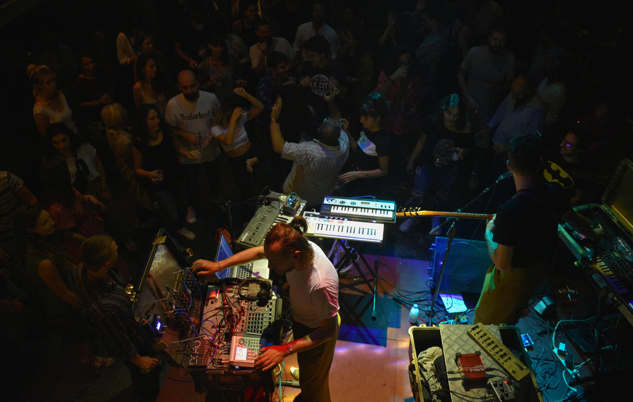 Concert animé avec des musiciens, des synthétiseurs et une foule dans une ambiance festive.