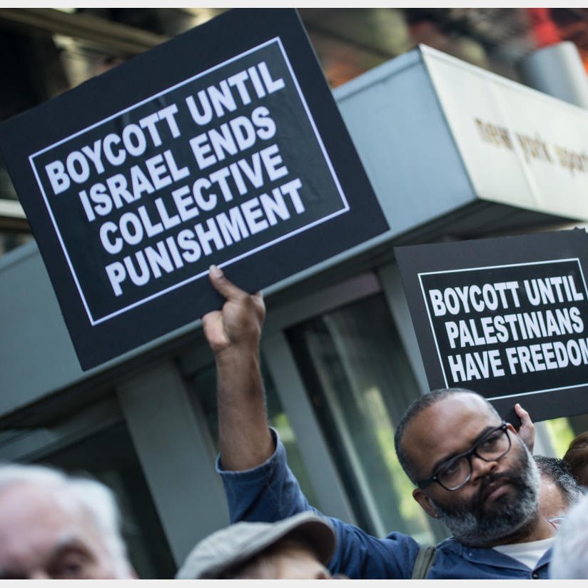 The image depicts a group of protesters holding signs at a demonstration. Some of the signs read "BOYCOTT UNTIL ISRAEL ENDS COLLECTIVE PUNISHMENT" and "BOYCOTT UNTIL PALESTINIANS HAVE FREEDOM." The atmosphere suggests a call for social justice and awareness regarding the Palestinian situation. The protesters appear engaged and determined in their stance.