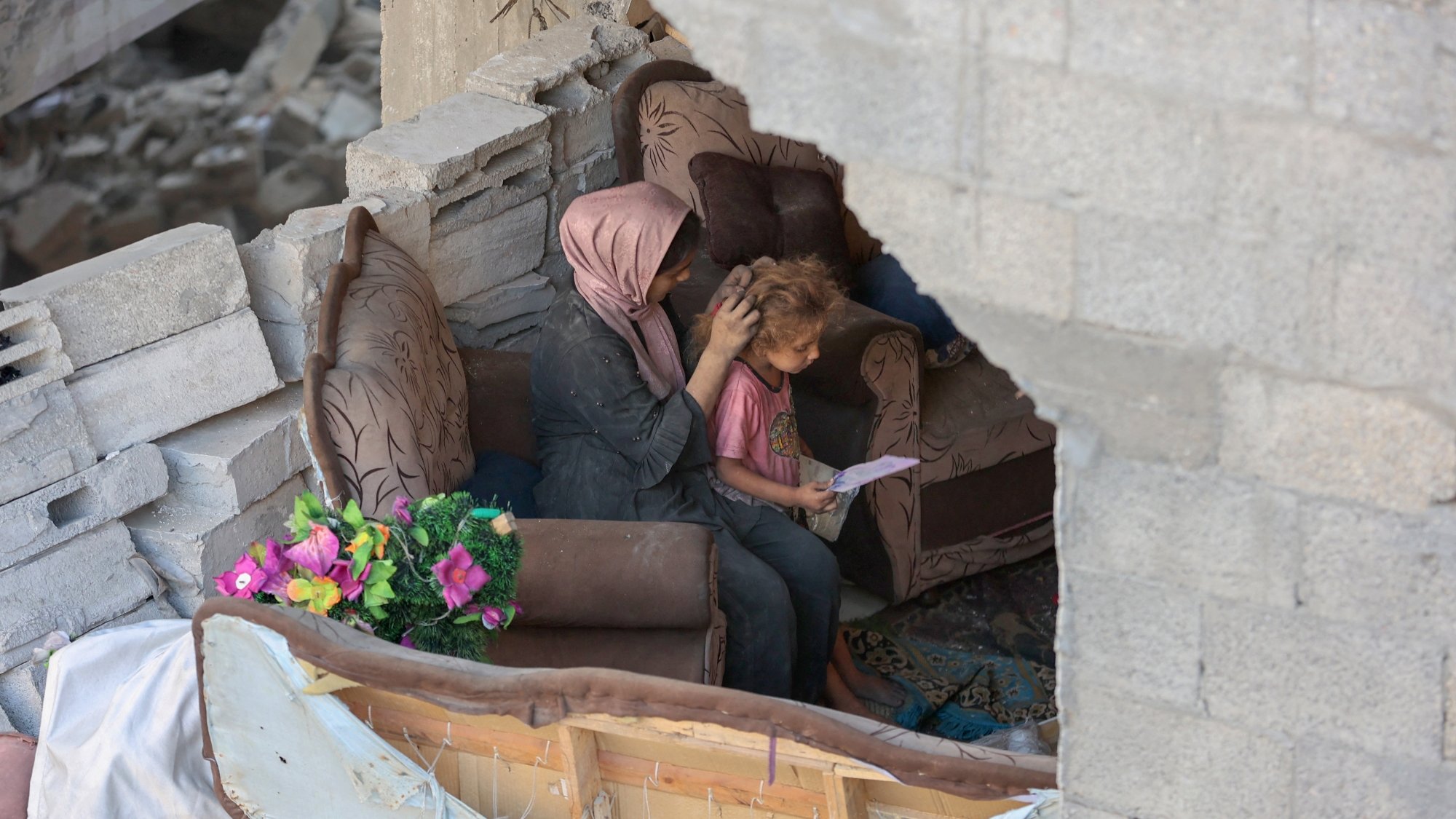 Une mère réconforte son enfant dans un espace endommagé, entourés de débris.
