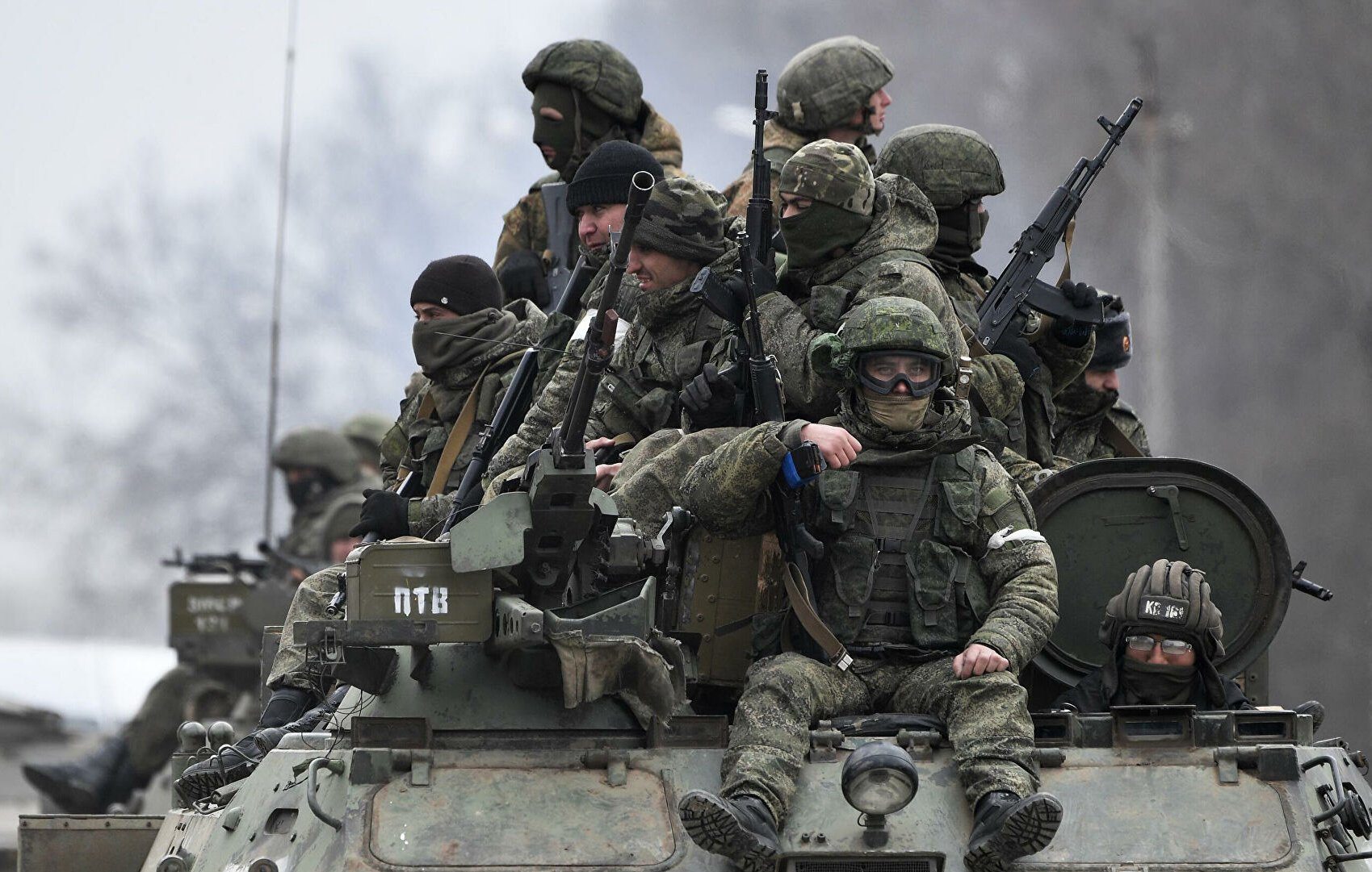 L'image montre un groupe de soldats armés, équipés de vêtements militaires et de casques, se tenant sur un véhicule blindé. Ils semblent en position attentive, probablement lors d'une opération militaire. L'ambiance est sérieuse et le paysage environnant est sombre, ce qui renforce le contexte militaire et opérationnel. Les soldats portent des masques et des lunettes, ce qui indique qu'ils sont préparés pour des conditions difficiles.