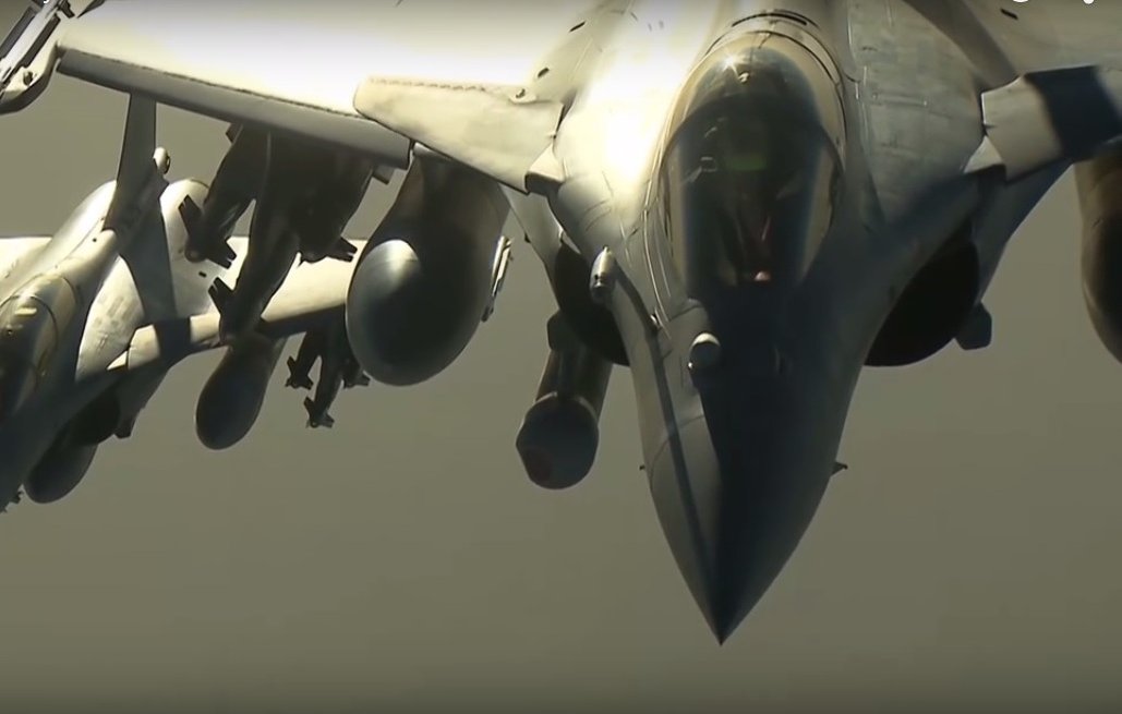 L'image montre plusieurs avions de chasse, probablement des Rafales, en formation dans le ciel. Les avions sont affichés de profil, mettant en valeur leur design aérodynamique. On peut observer leurs ailes, leurs moteurs et les divers équipements militaires qui les équipent. Le ciel semble clair, ce qui permet une bonne visibilité des avions. L'ensemble donne une impression de puissance et de précision technologique.