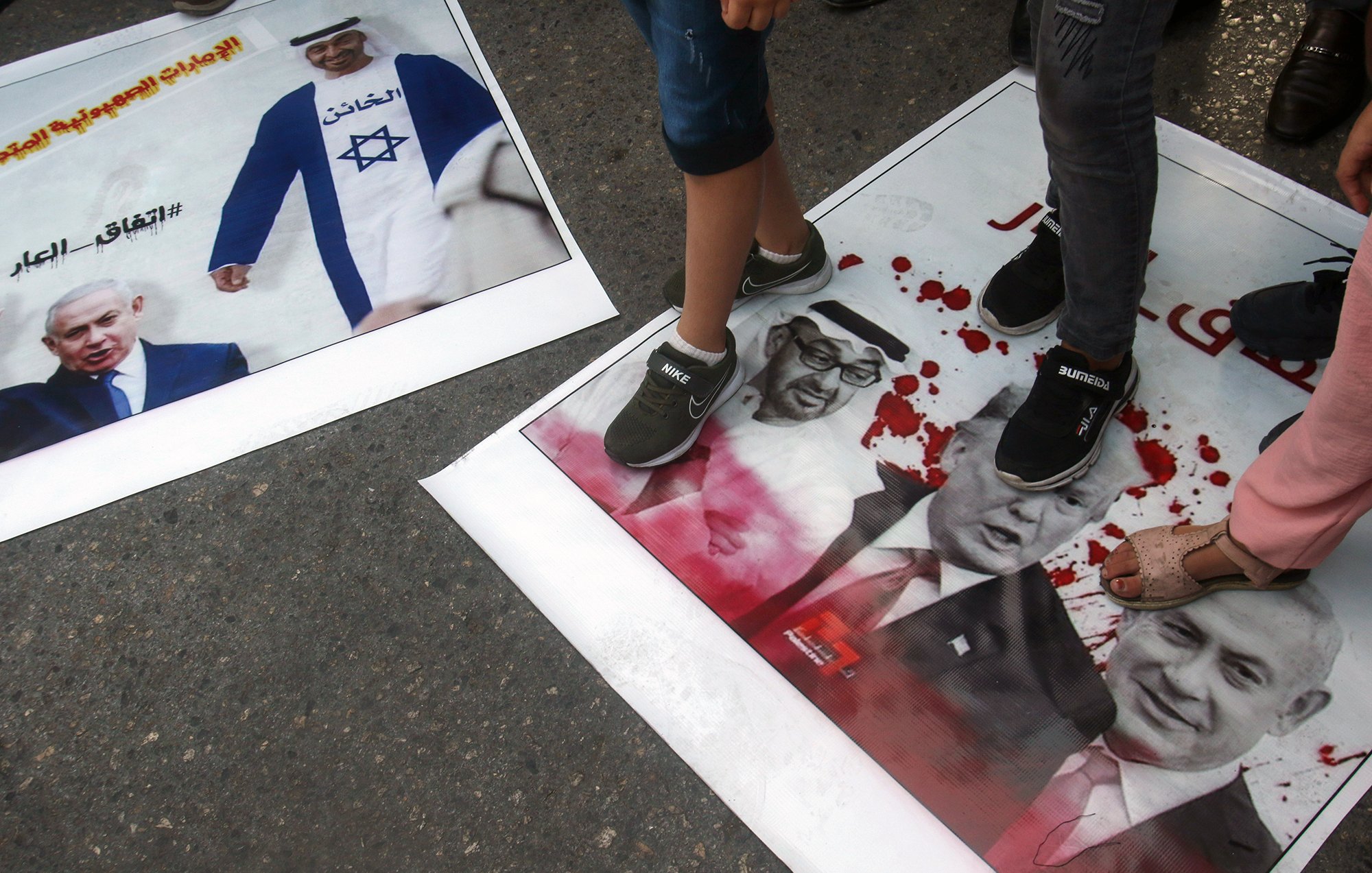 L'image montre des affiches au sol sur lesquelles sont piétinées des images de personnalités politiques, notamment Benjamin Netanyahu, Donald Trump et d'autres figures. Les affiches semblent être liées à une manifestation ou une protestation, avec des couleurs vives et des motifs qui attirent l'attention. Les personnes présentes dans l'image sont en train de marcher dessus, suggérant une attitude de rejet ou de mécontentement envers ces figures. Les tonnerres de couleurs et le contenu des affiches pourraient refléter des sentiments politiques forts.