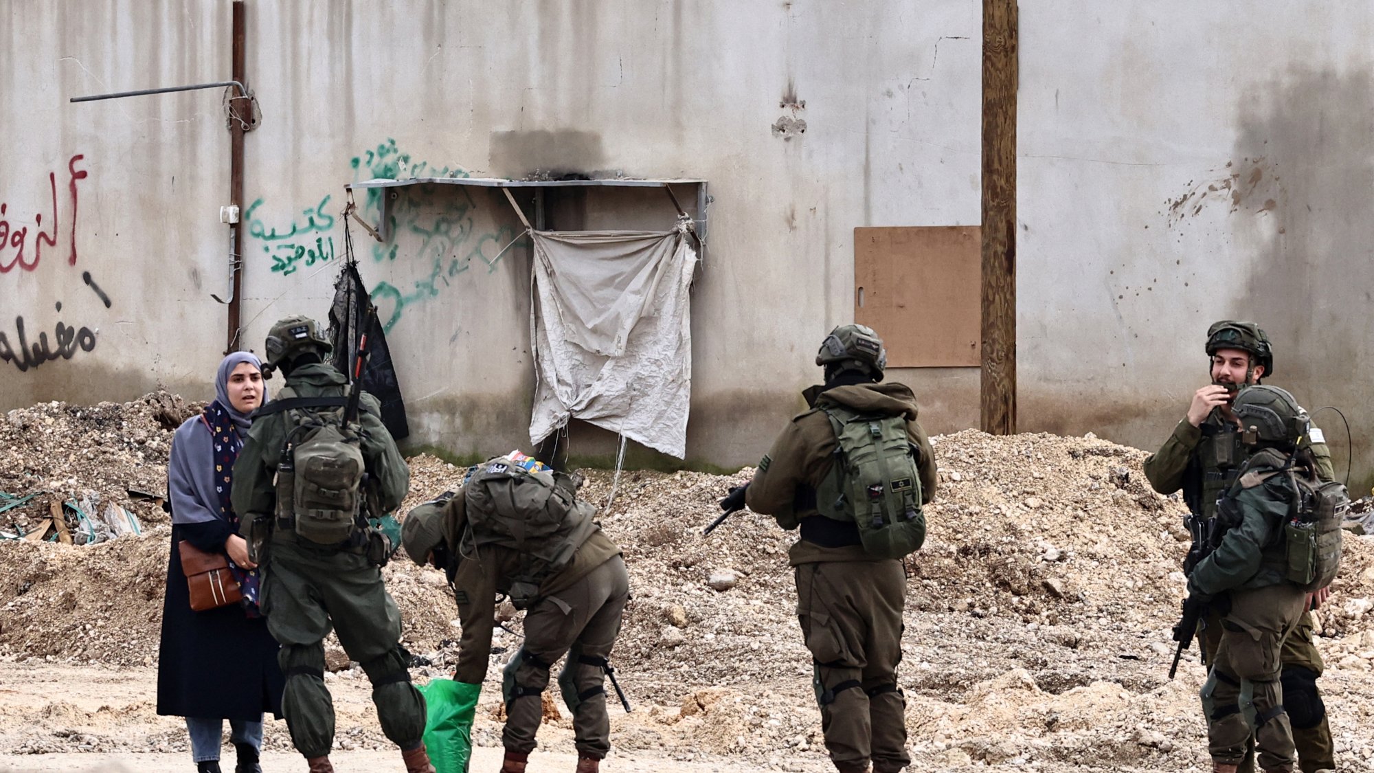 Soldiers in military gear interact with a woman in an urban setting, surrounded by debris.