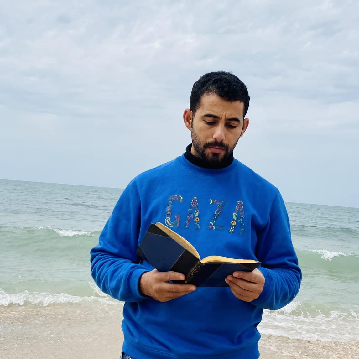 در این تصویر، مردی در کنار دریا ایستاده است و یک کتاب در دست دارد. او لباسی آبی رنگ به تن دارد که روی آن کلمه "GAZA" به چشم می‌خورد. پس‌زمینه تصویر را دریای آرام و آسمانی ابری تشکیل می‌دهد. موج‌های دریا به ساحل می‌رسند و فضای آرامی را به تصویر بخشیده‌اند. 