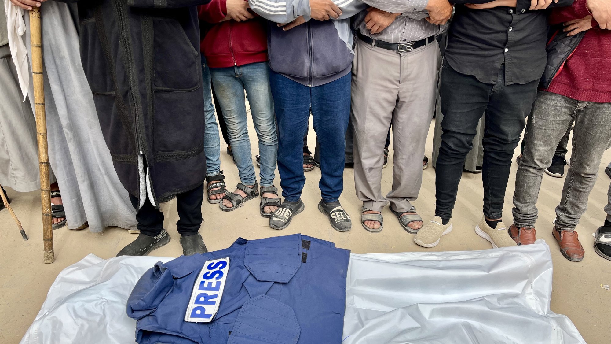 Gruppo di persone in piedi attorno a una giacca con scritto "PRESS" su un telo.