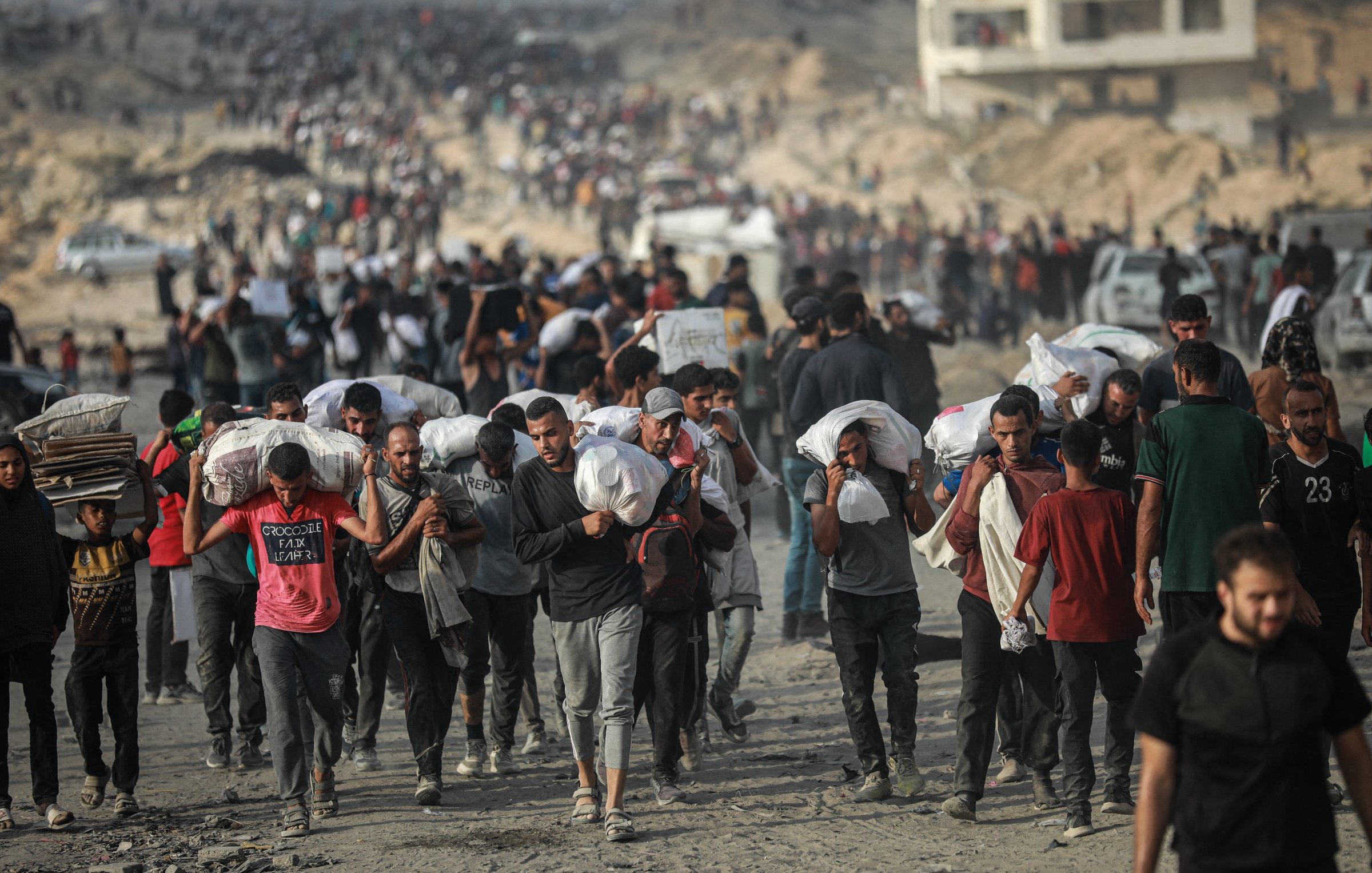 Des personnes marchent en masse, portant des charges sur leurs épaules, dans un environnement difficile.