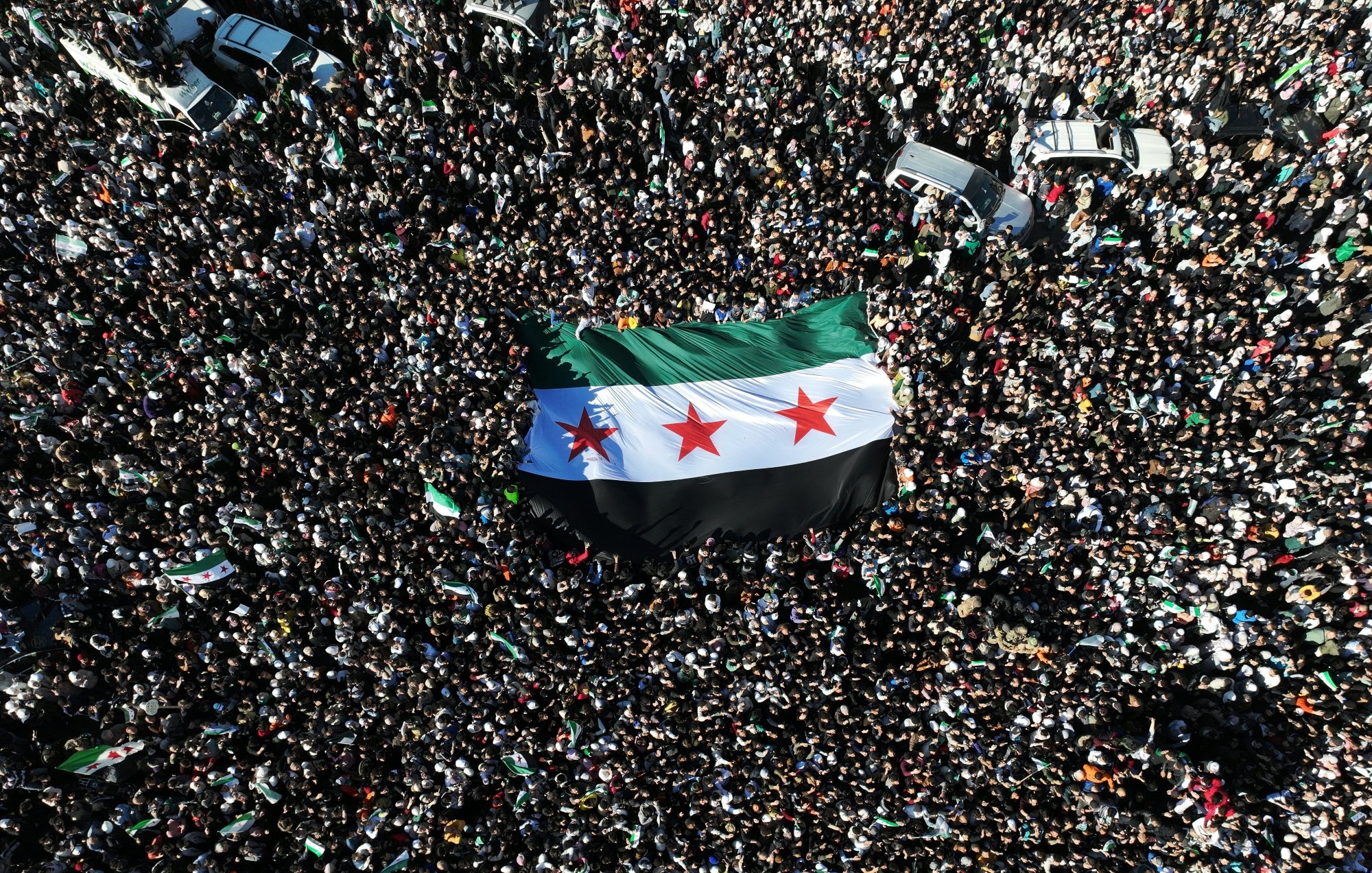 Una grande folla con una bandiera siriana al centro.