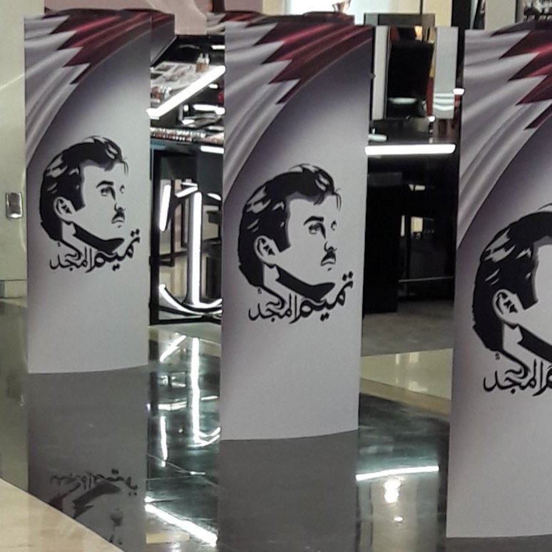 L'image montre plusieurs panneaux verticaux disposés en ligne. Chaque panneau présente un motif similaire, avec un fond qui semble afficher des couleurs en dégradé, accompagnés d'une illustration d'un homme avec une moustache. Sur les panneaux, on peut également observer des éléments de texte en arabe. L'ensemble donne une impression moderne et artistique, probablement lié à un événement ou une exposition.