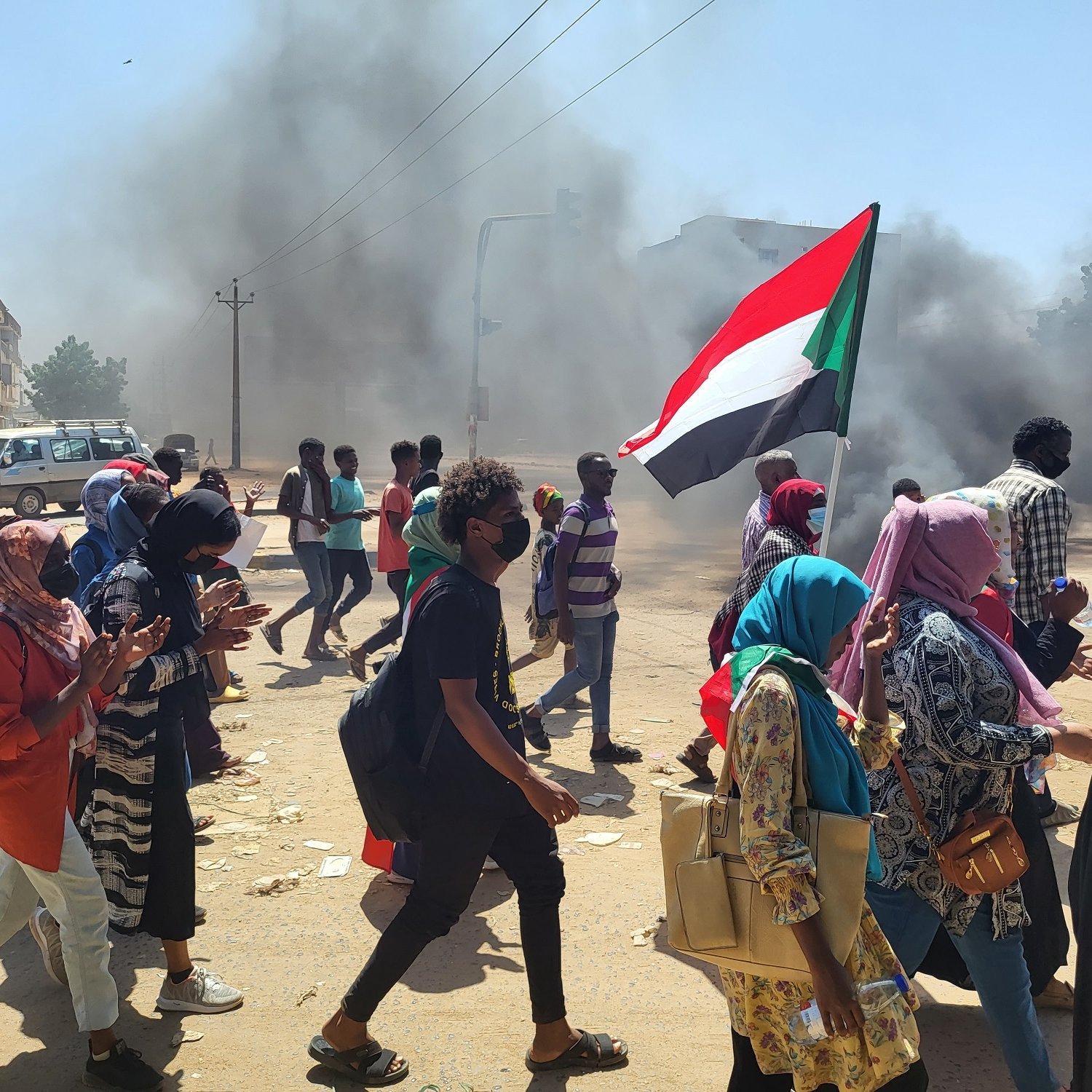 Manifestation dans la rue, fumée, drapeau soudanais, personnes marchant ensemble.