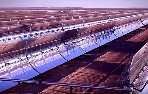 L'image montre un paysage d'énergie solaire, probablement un champ de miroirs ou de panneaux solaires. On peut voir plusieurs lignes de miroirs courbés, orientés vers le soleil. Ces miroirs concentrent les rayons solaires pour produire de l'énergie. L'arrière-plan est désertique ou plat, suggérant que l'installation est située dans une région ensoleillée. L'ambiance générale évoque une technologie moderne et des initiatives en faveur des énergies renouvelables.