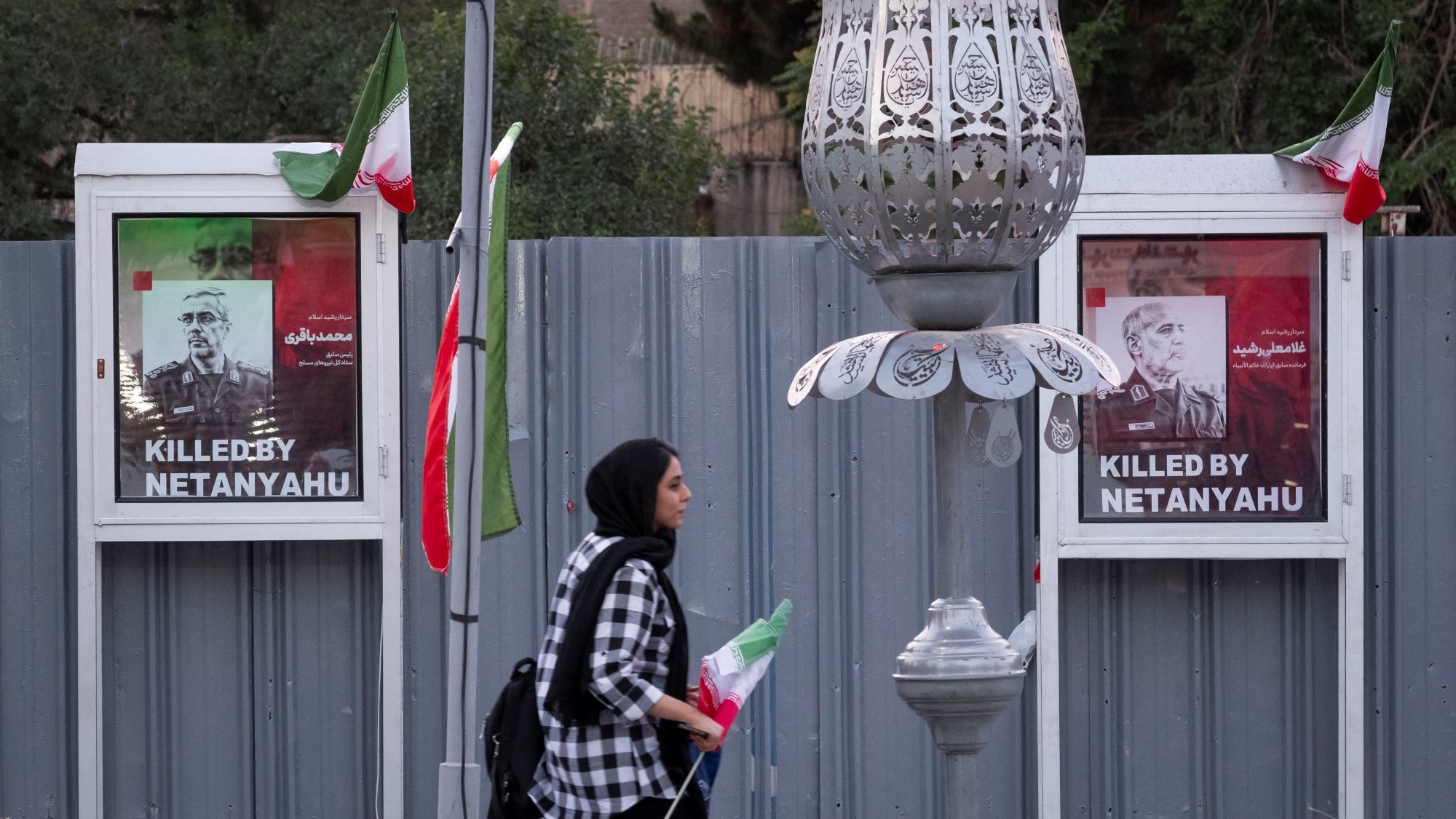 Deux affiches de victimes avec le texte "Killed by Netanyahu", une femme passe avec un drapeau.