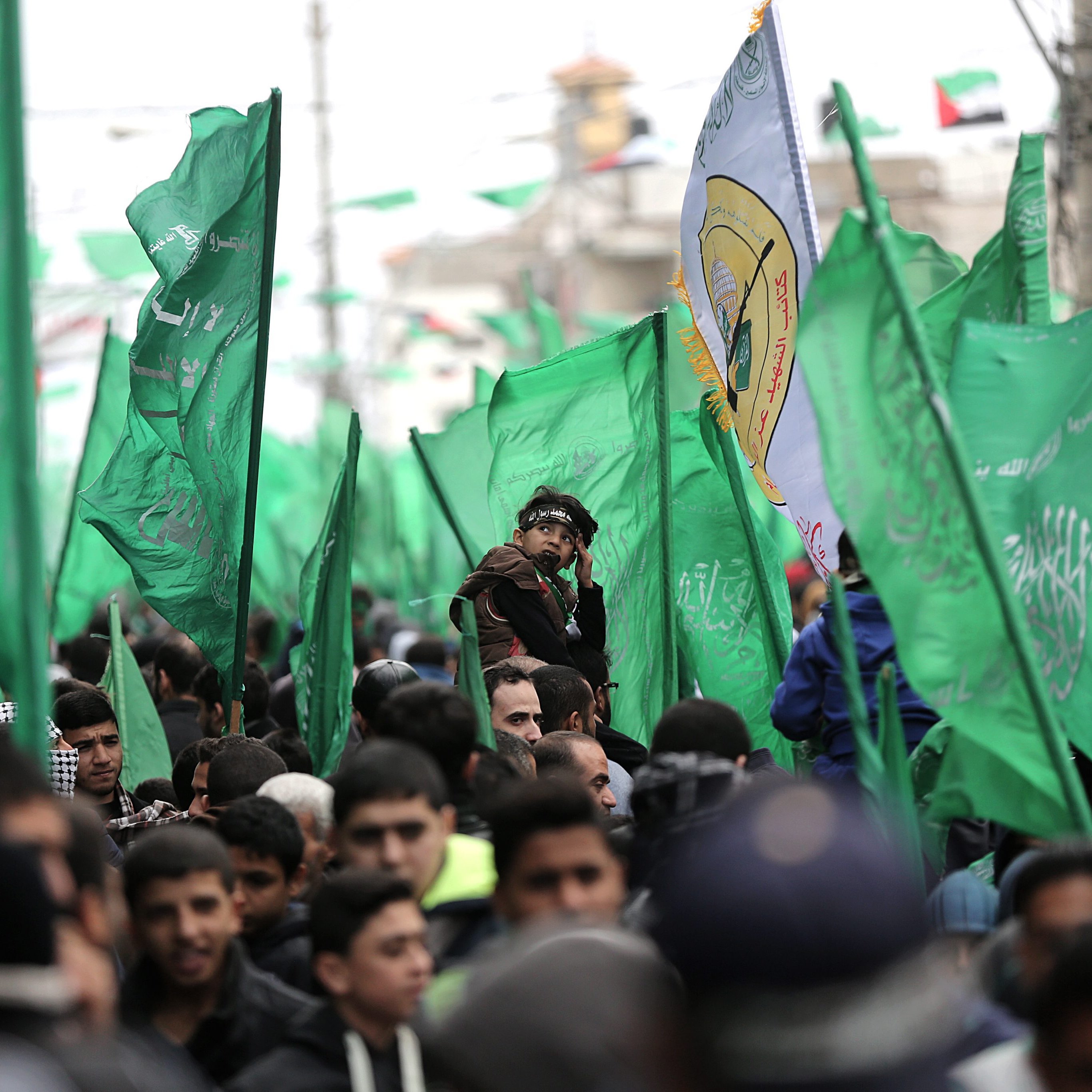 L'image montre une foule lors d'un rassemblement, où de nombreuses personnes portent des drapeaux verts. Les drapeaux semblent représenter un mouvement ou un groupe politique. Au premier plan, on observe un enfant sur les épaules d'un adulte, ce qui suggère une atmosphère de célébration ou de protestation. L'arrière-plan est rempli de personnes, renforçant l'idée d'un événement collectif. L'ambiance générale semble dynamique et engagée.