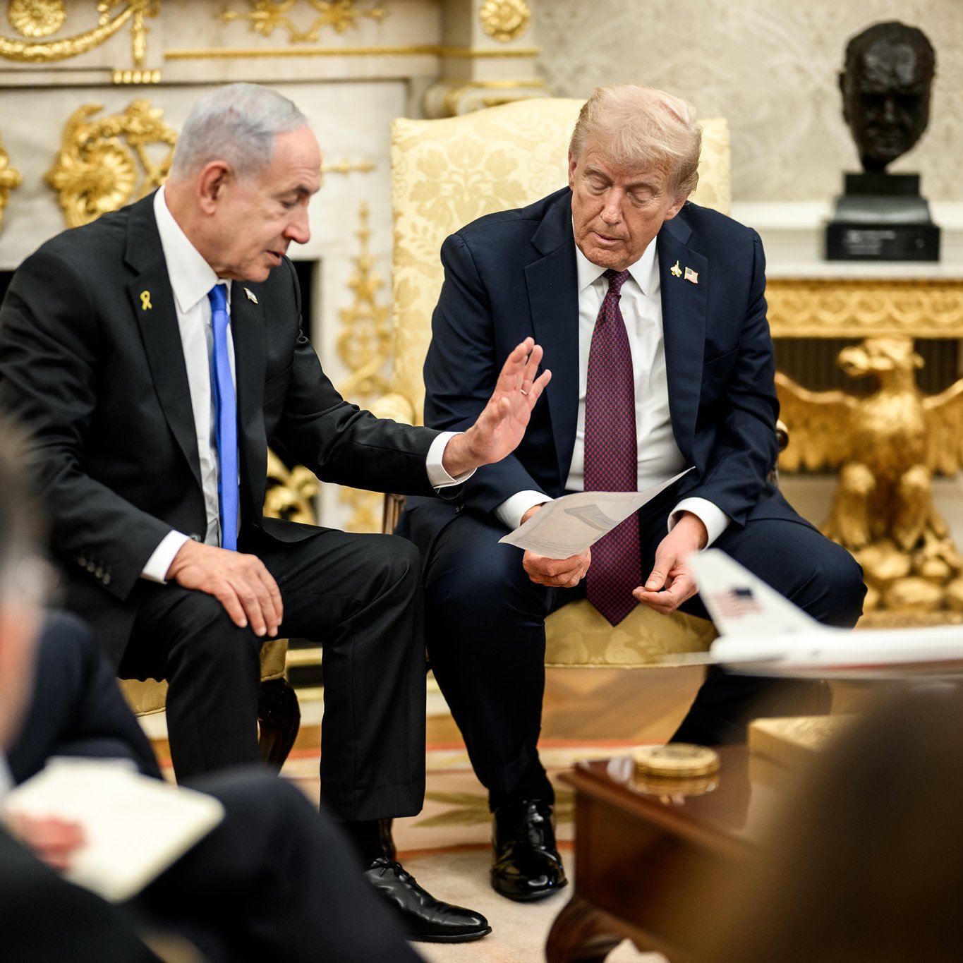 Deux hommes en costume discutent assis dans un bureau au mobilier élégant.