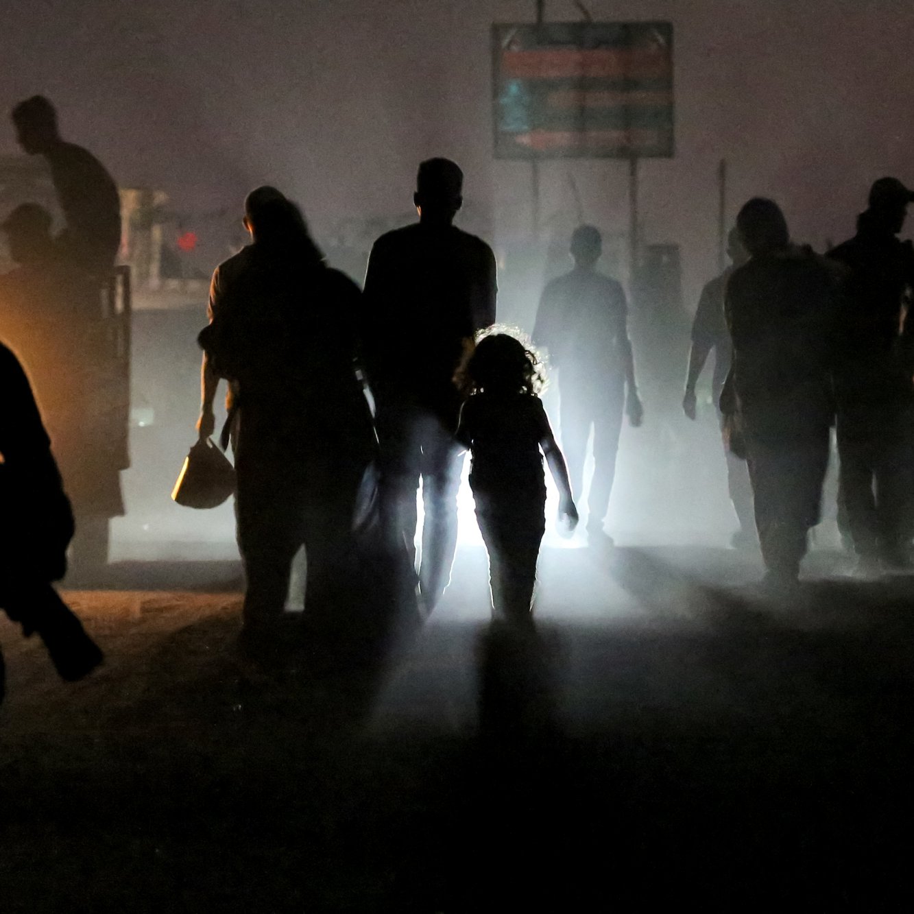Silhouettes of people walk through fog; a child stands out in the light, creating a striking contrast.