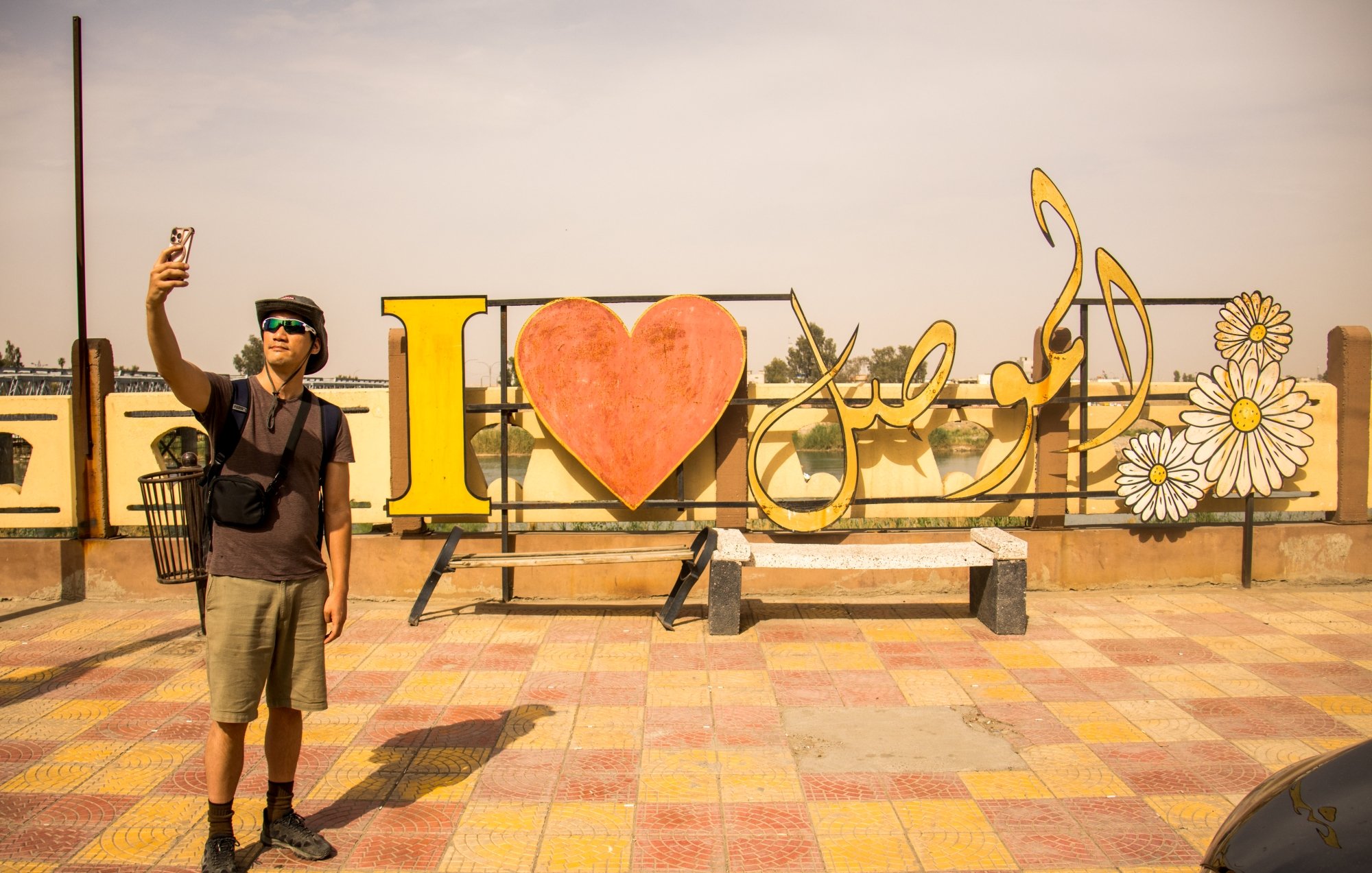 Un homme prend un selfie devant une grande inscription colorée "I ❤️ [nom]".